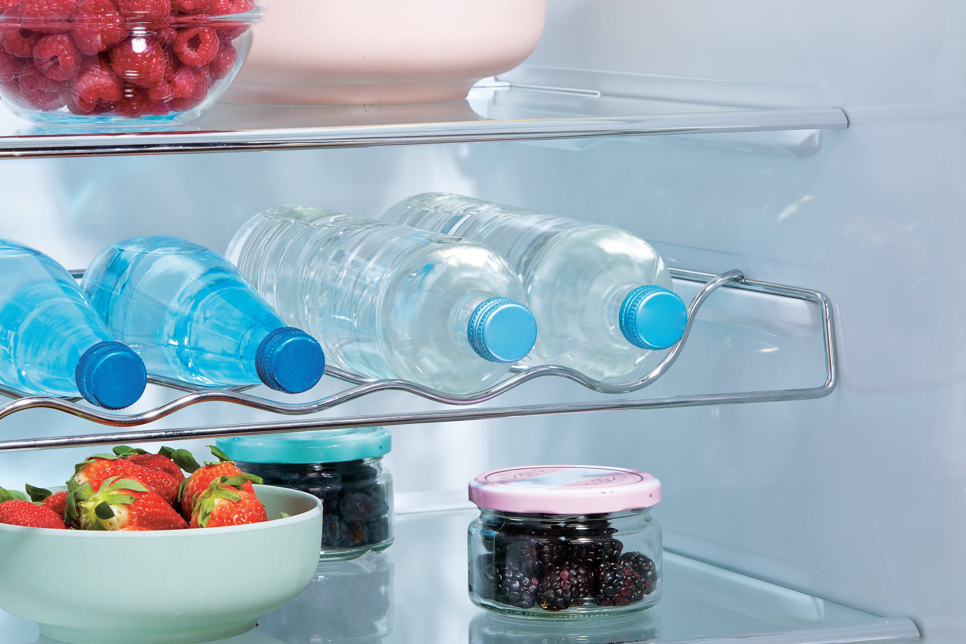 Interno del frigorifero con ripiani. Contiene bottiglie d'acqua, bacche in ciotole, per conservare il cibo.