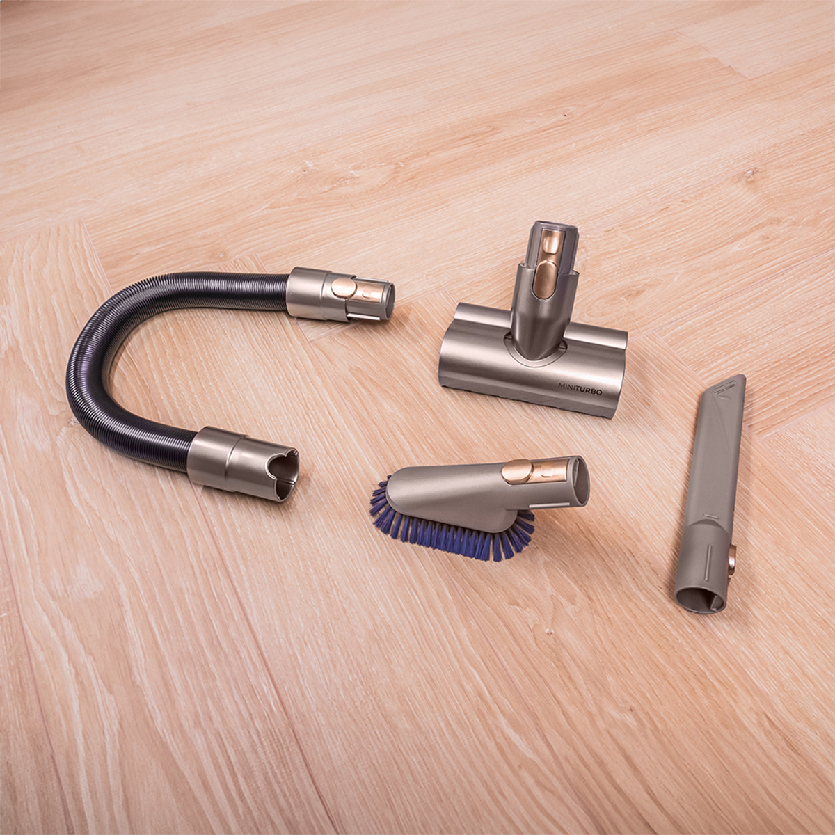 Accesorios de aspiradora en suelo de madera. Incluye manguera, cepillo y otras dos herramientas.