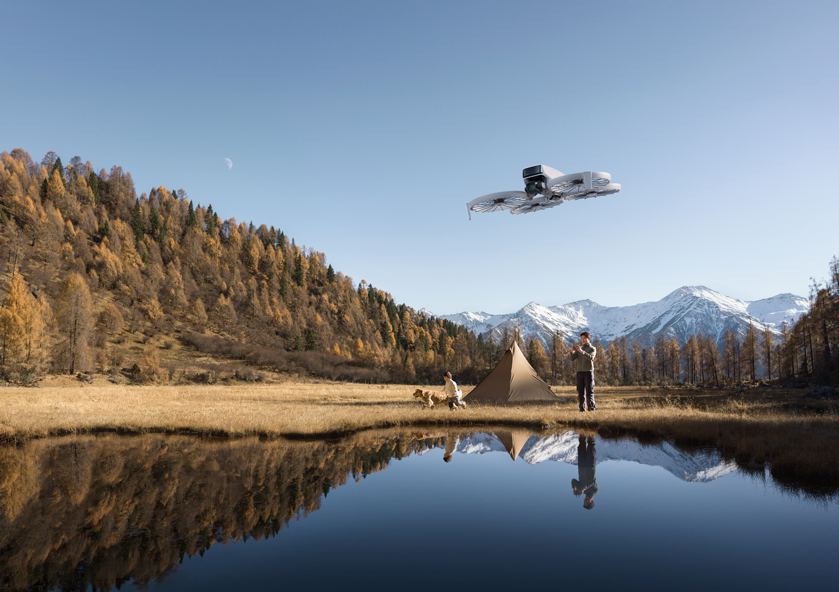 Drohne am Himmel über einem See. Menschen, Hund, Zelt und Berge im Hintergrund.