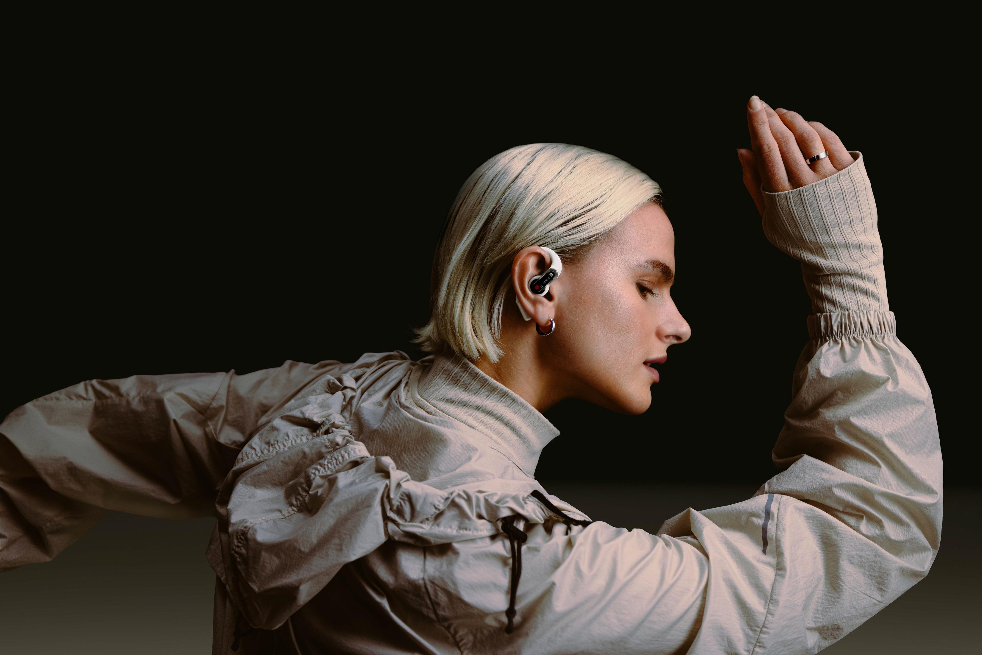 Kobieta w beżowym stroju do biegania ze słuchawką do biegania. Ciemne tło.