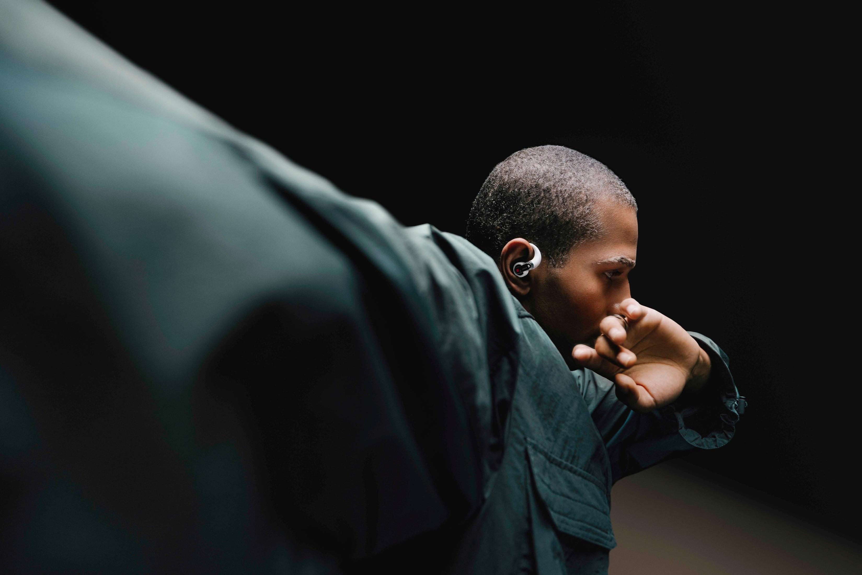 Osoba nosząca słuchawki, patrząca na bok, z ciemnym tłem.