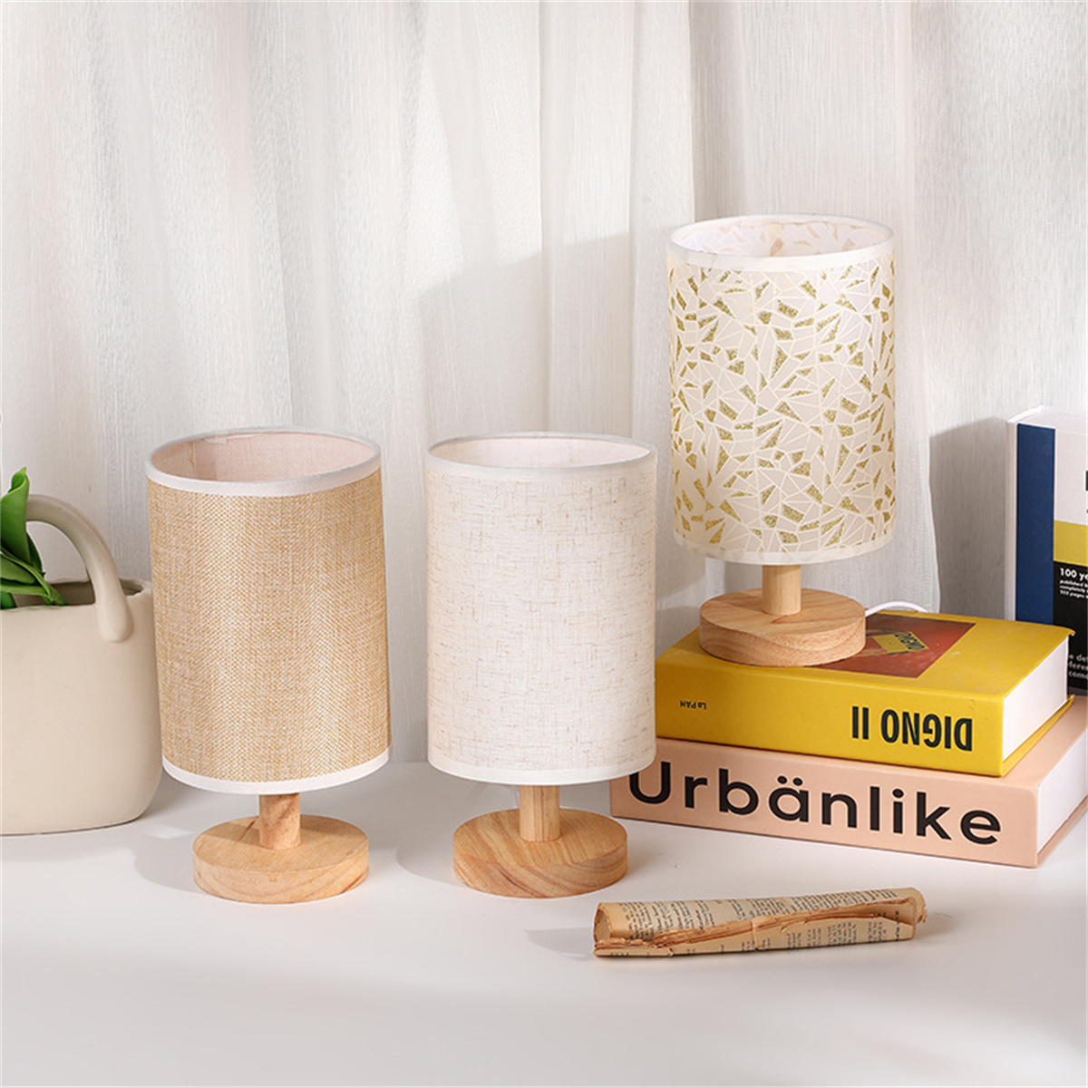 Drei Lampen mit verschiedenen Schirmen: beige, weiß und gold gemustert. Auf weißer Oberfläche platziert.