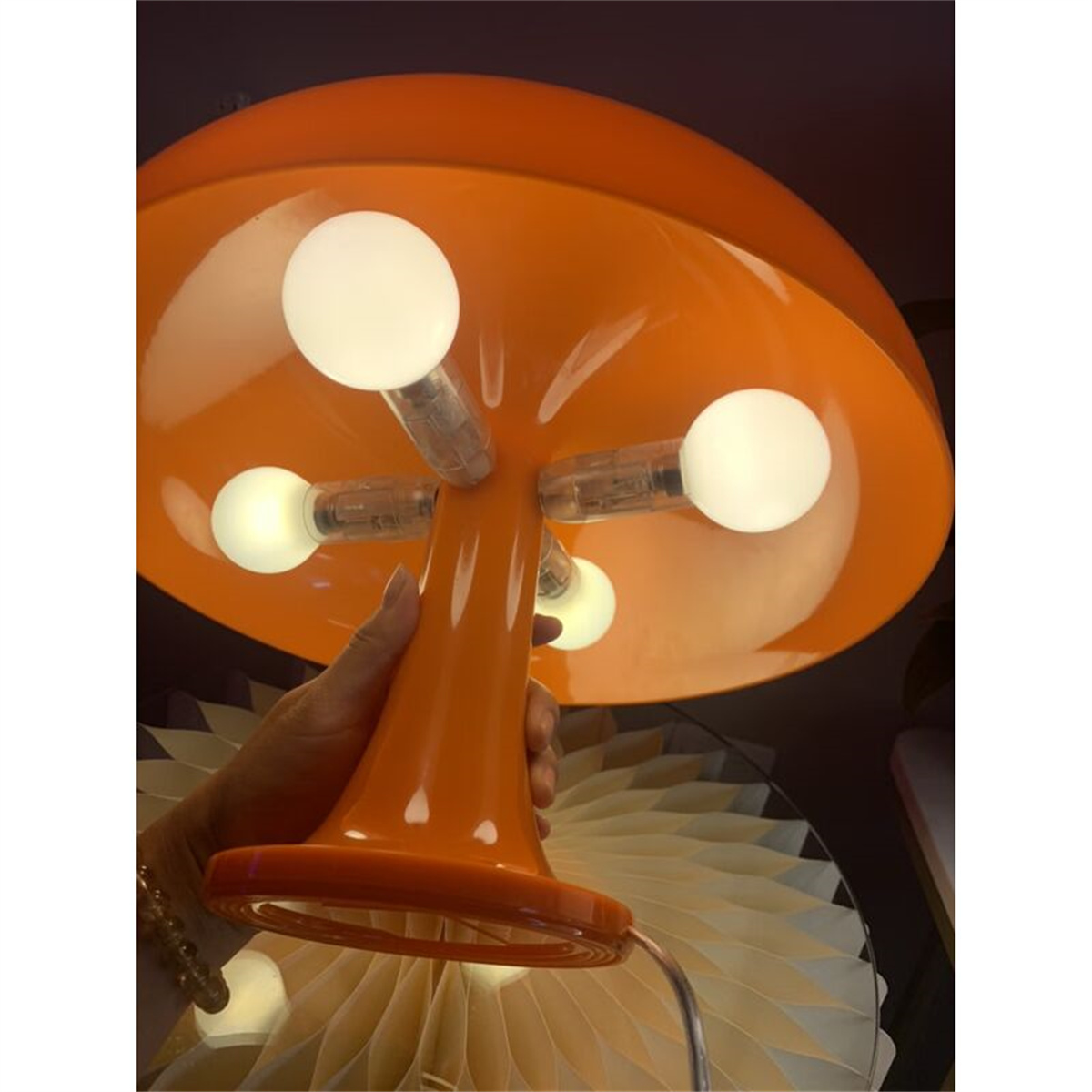 Orangefarbene pilzförmige Lampe mit vier Glühbirnen und einer Hand, die sie hält.
