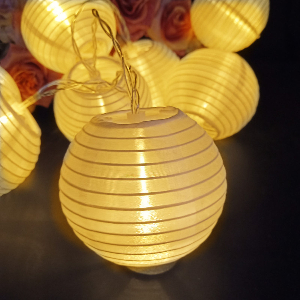 Eine Lichterkette mit beleuchteten Papierlaternen. Rund, weiß, gestreift. Dunkler Hintergrund.