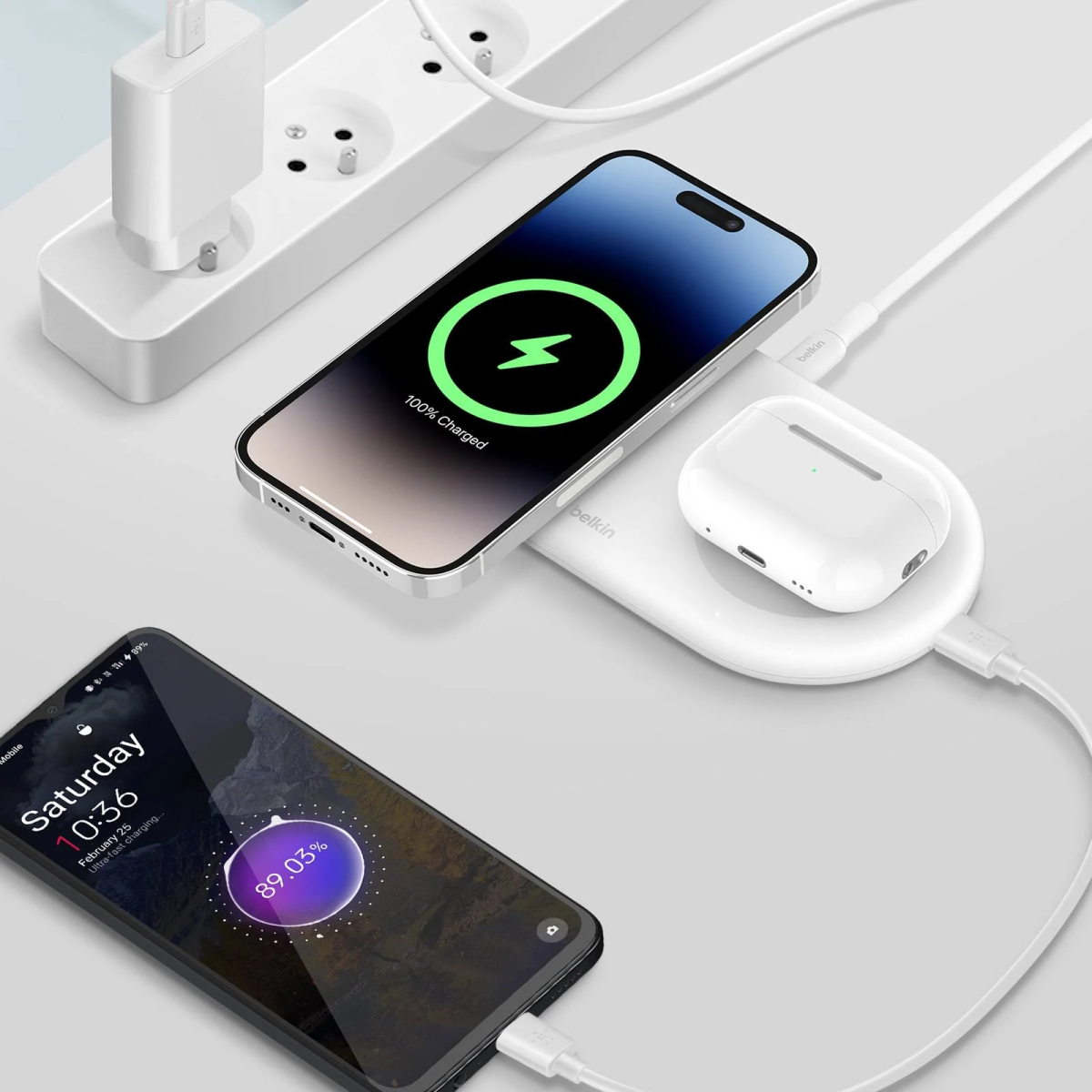 Due telefoni e una custodia per auricolari in carica su un pad di ricarica wireless bianco, su una scrivania.