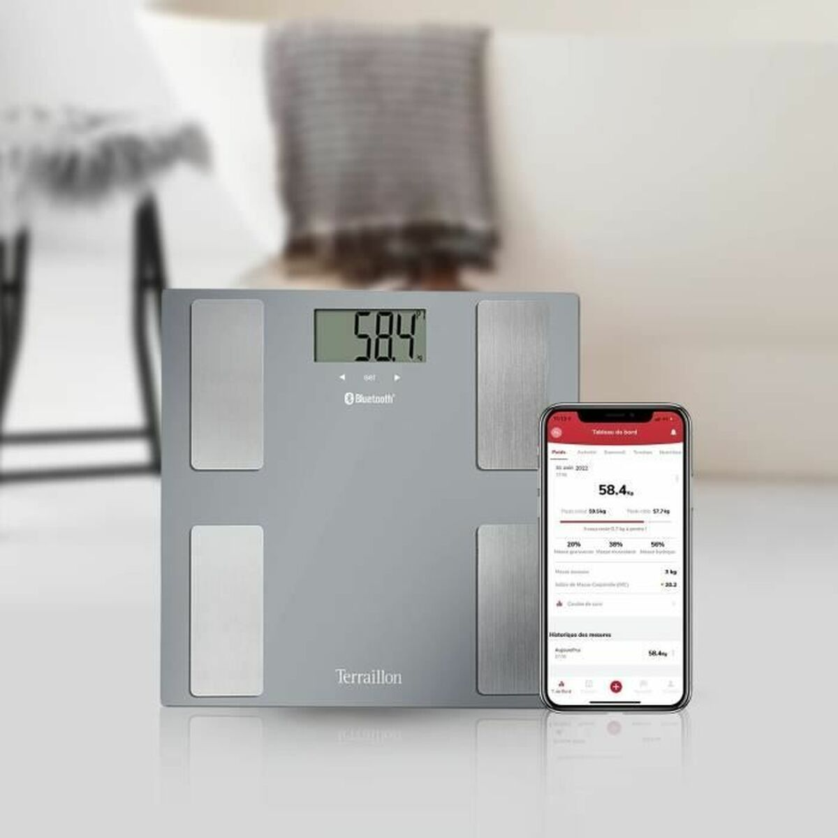 Báscula inteligente con pantalla mostrando 58.4 y smartphone con datos de peso. Superficie blanca.