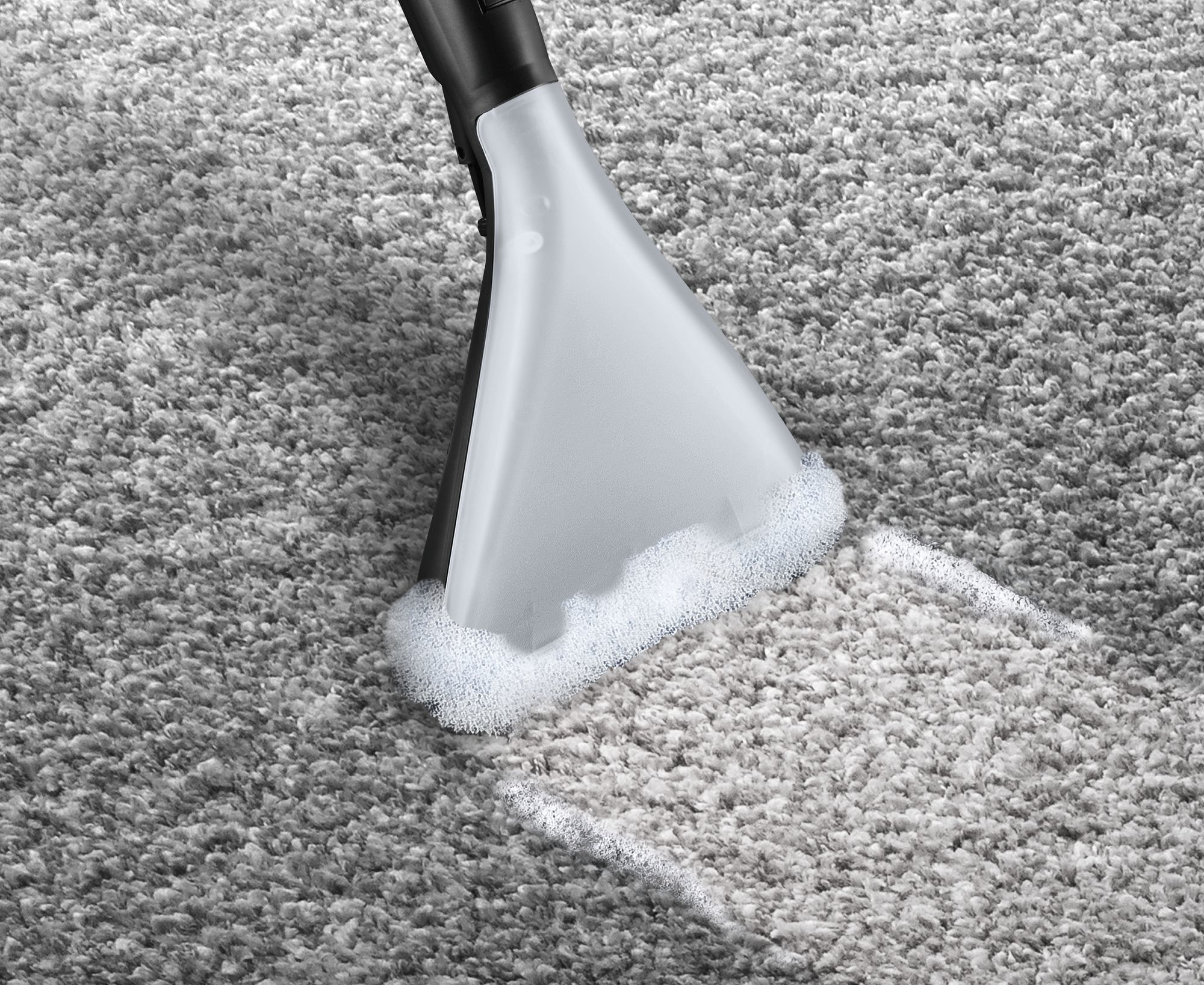 Zbliżenie głowicy odkurzacza czyszczącej szary dywan, z pianą.