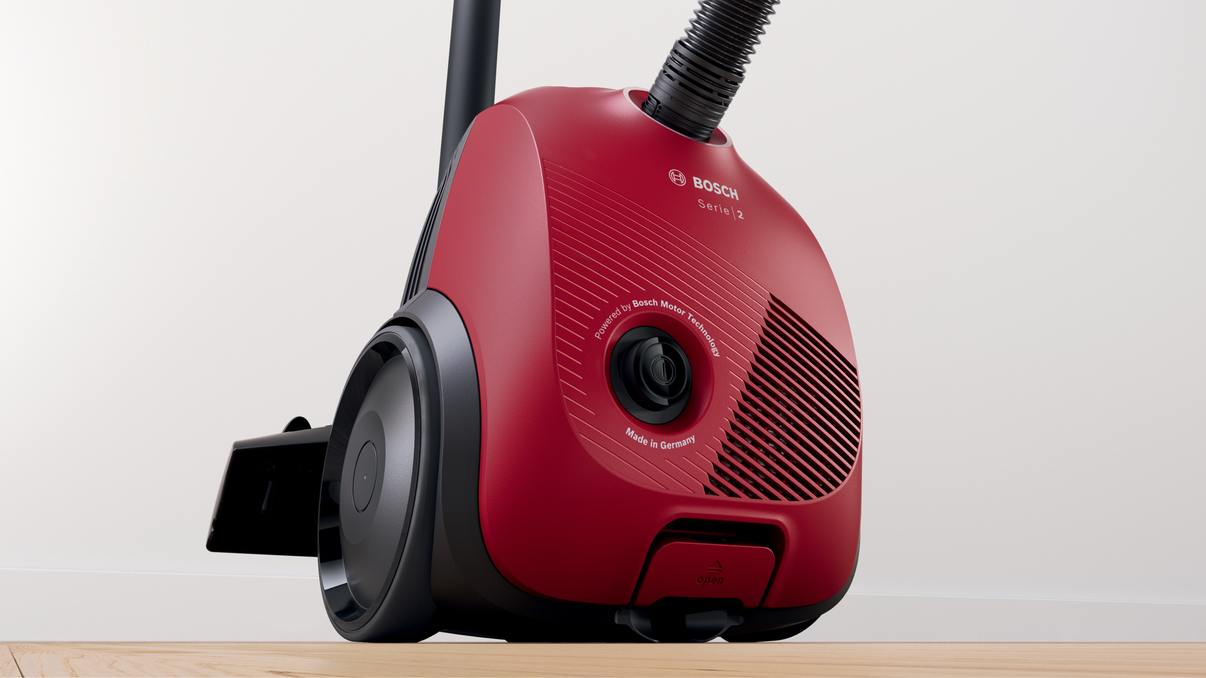 A red Bosch Series 2 vacuum cleaner, shown close-up on a wooden floor against a white wall background.