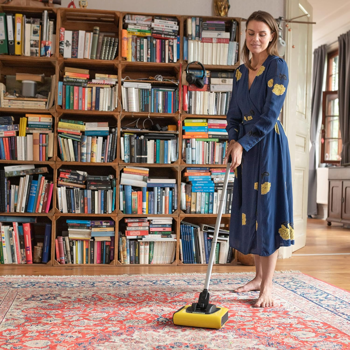 Una donna in un vestito blu aspira un tappeto rosso davanti a una libreria.