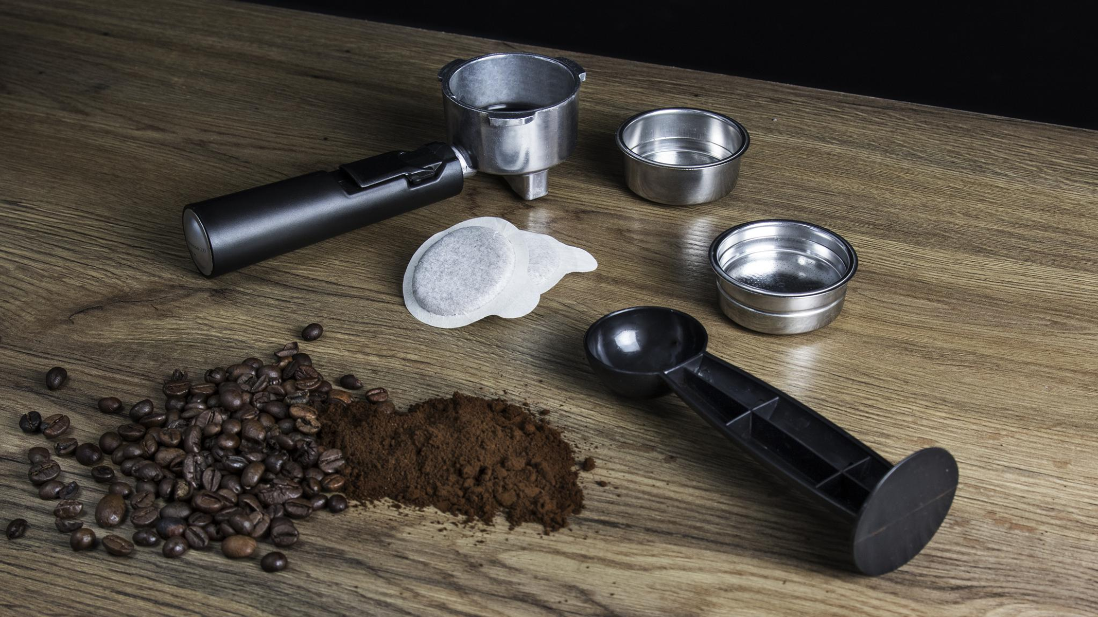 Parti della macchina per caffè espresso su legno: portafiltro, filtri, caffè macinato, chicchi e cucchiaio.