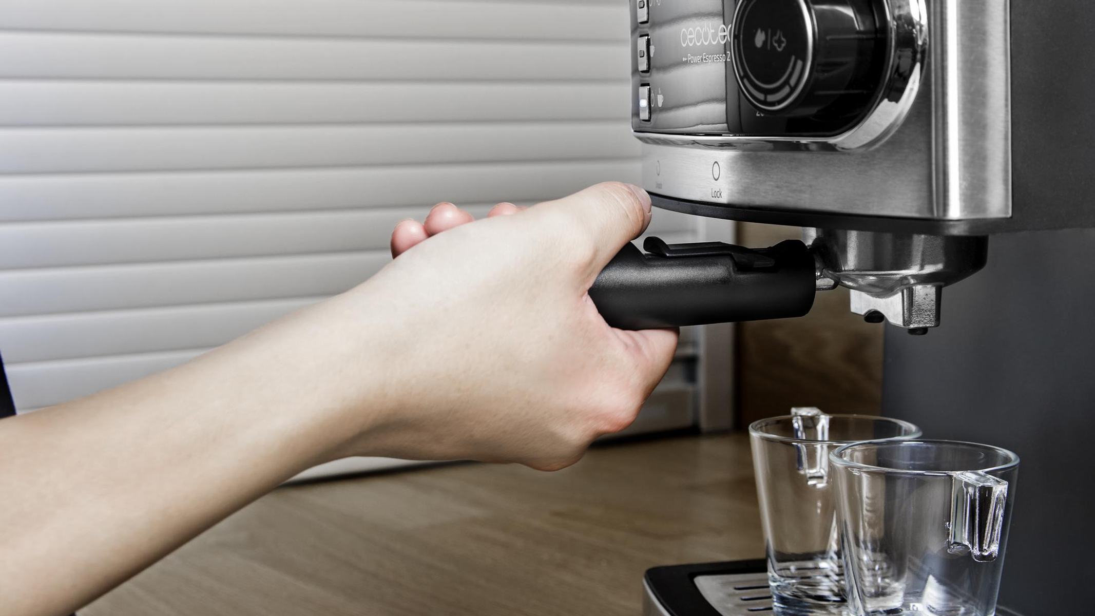 Una mano inserisce un portafiltro in una macchina per espresso. Due bicchieri sono sotto l'erogatore.