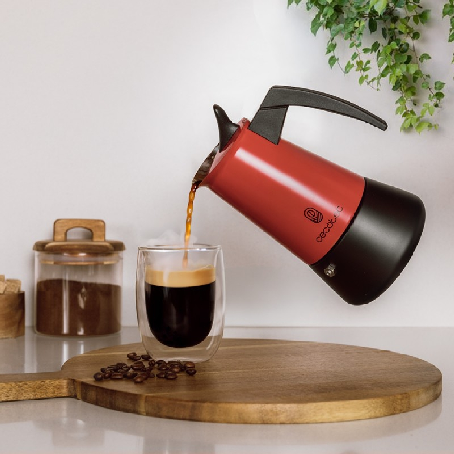 Kaffee wird aus einer rot-schwarzen Mokkakanne in ein Glas gegossen. Kaffeebohnen und Holzbrett auch gezeigt.