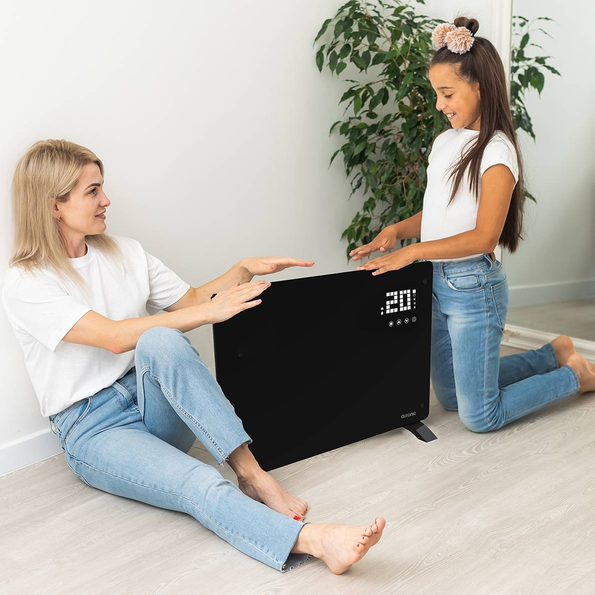 Een vrouw en een meisje zitten naast een zwarte heater. Ze raken de heater aan.