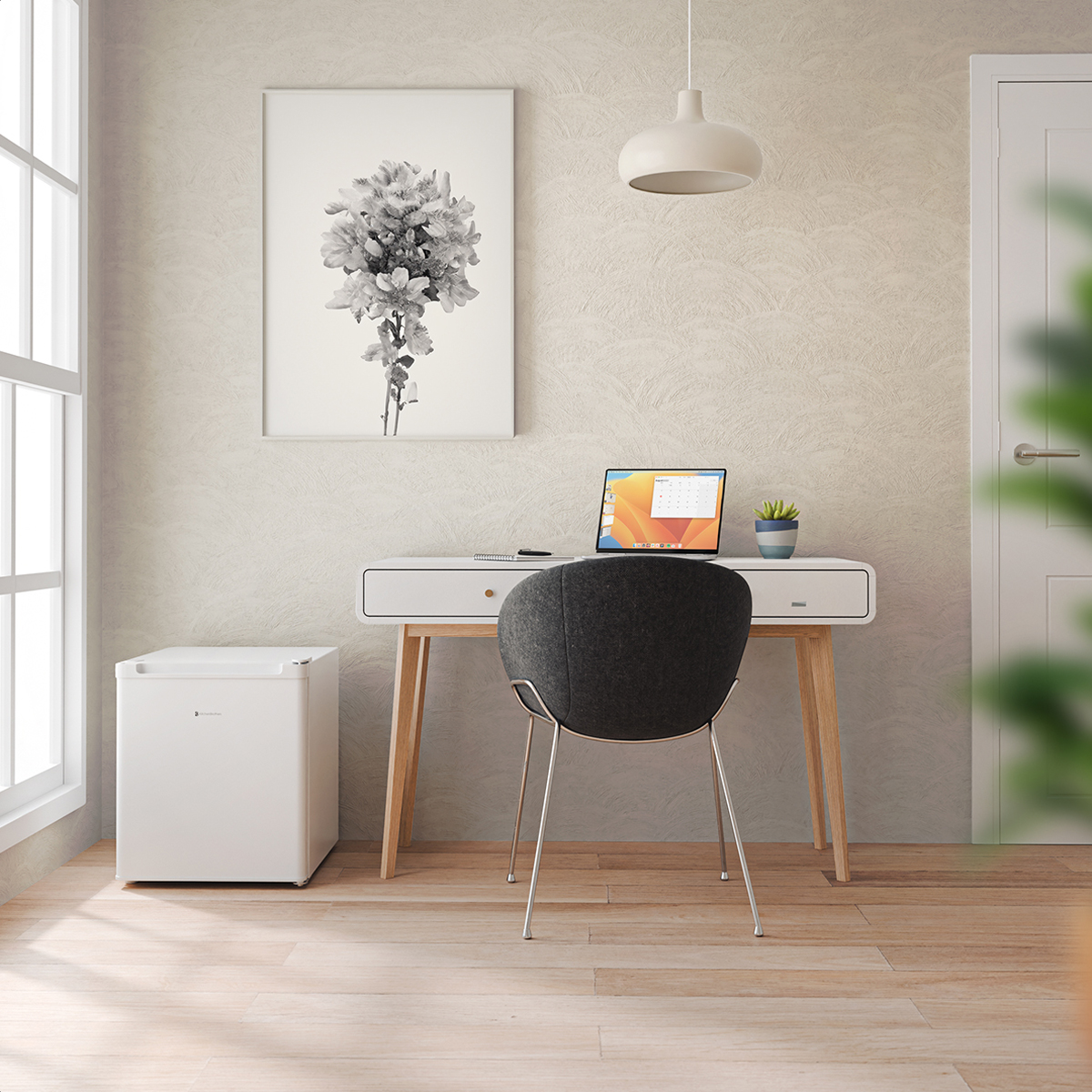 A desk with a laptop, a small fridge, and a picture frame.