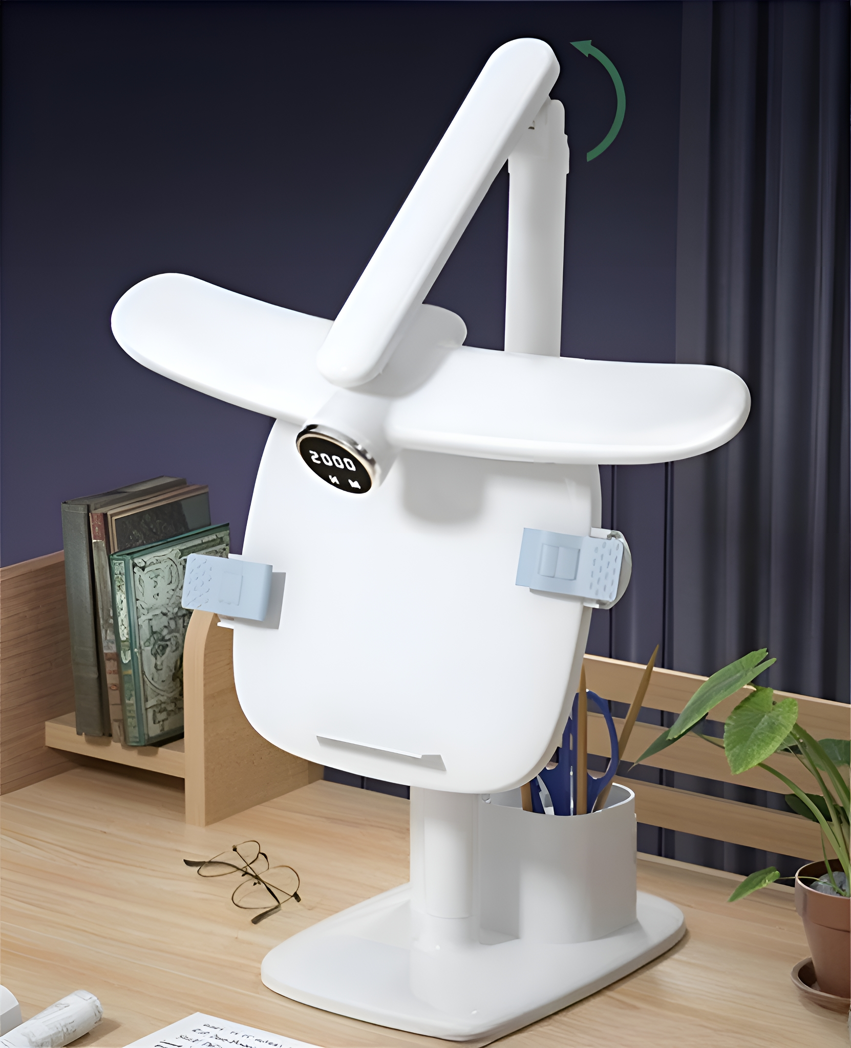 Weiße Schreibtischlampe mit verstellbarem Kopf und Fuß, auf einem Holztisch mit Büchern und einer Pflanze.