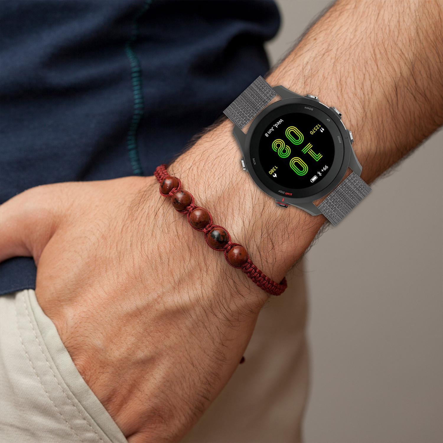 Mężczyzna noszący smartwatch na nadgarstku i czerwoną bransoletkę z koralików, na beżowym tle.