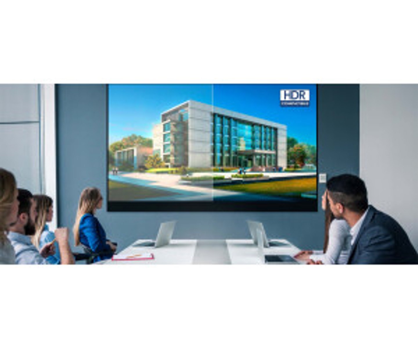 Ludzie w sali konferencyjnej patrzą na ekran z obrazem budynku.