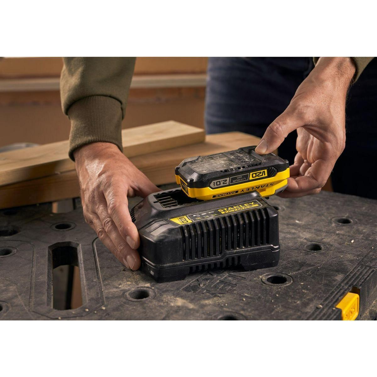 Manos colocando una batería en un cargador. Colores negro y amarillo. Mesa de madera.