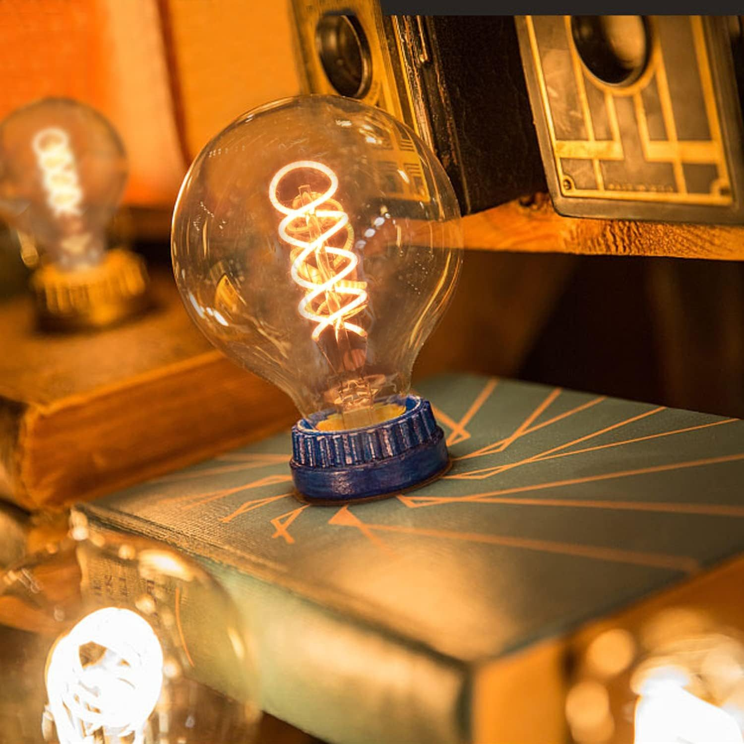Una lampadina accesa su un libro con altri libri e una fotocamera sullo sfondo.