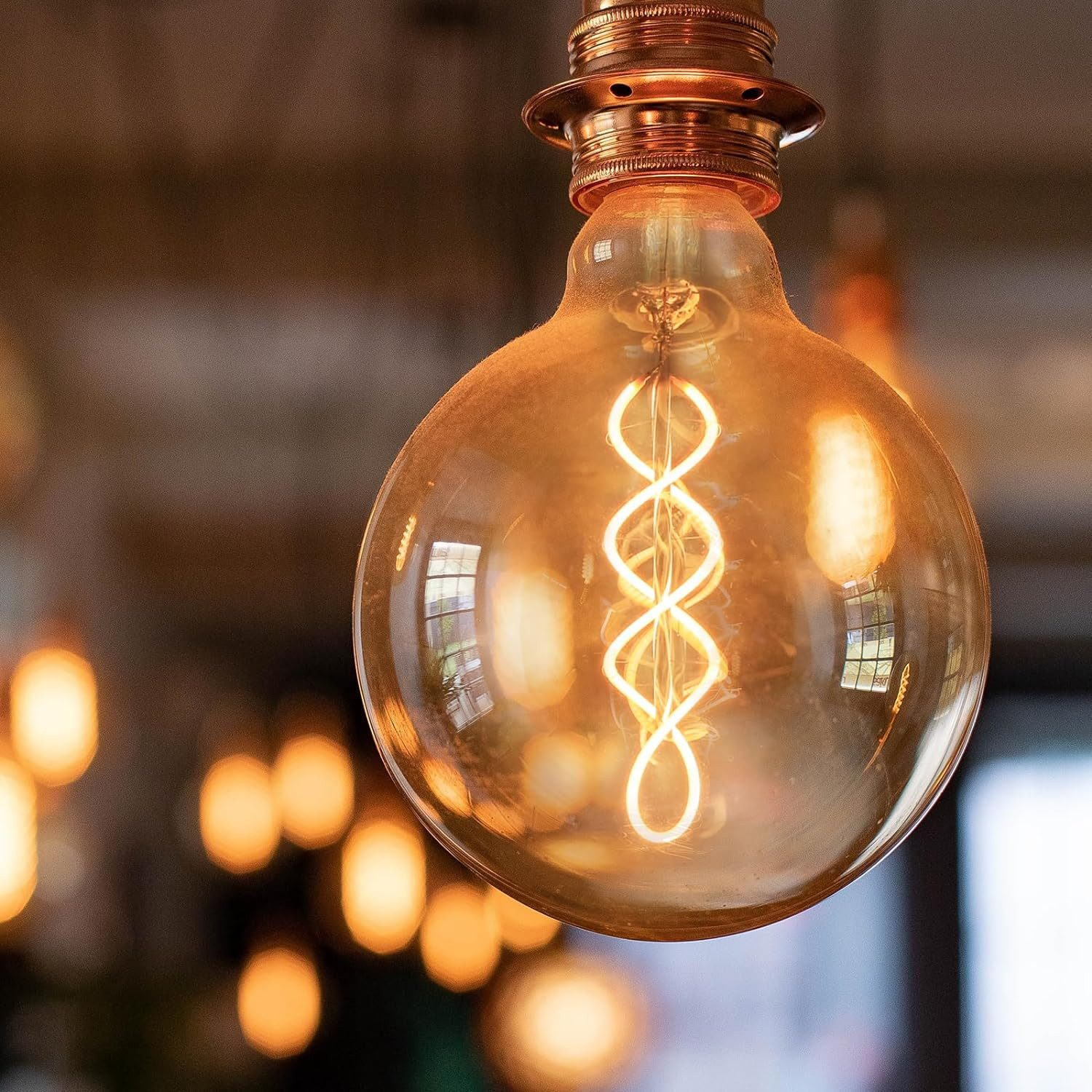 Primo piano di una lampadina dorata illuminata con filamento a spirale, su sfondo sfocato.