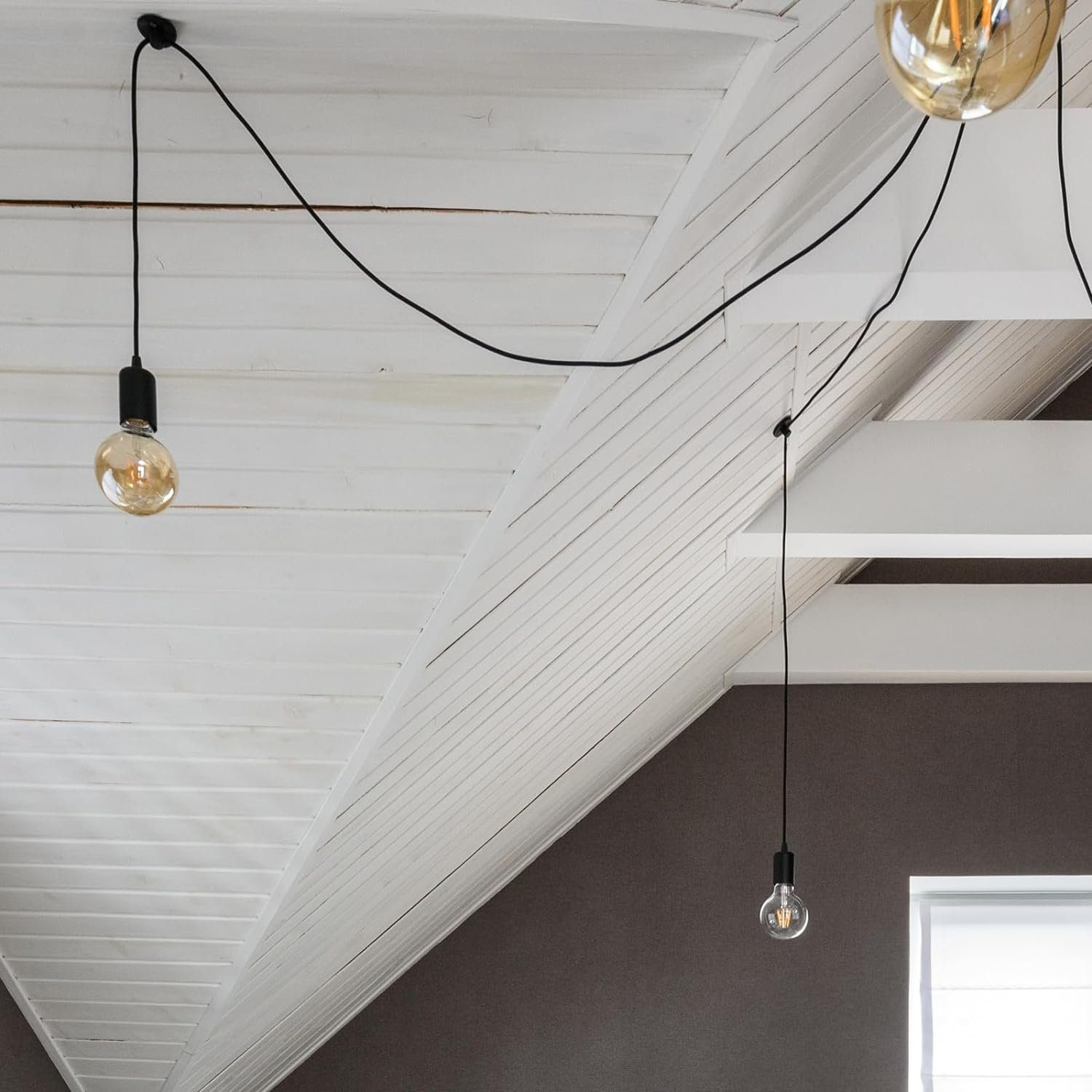 Un soffitto bianco con travi in legno e tre lampadine appese. Il muro è grigio scuro.