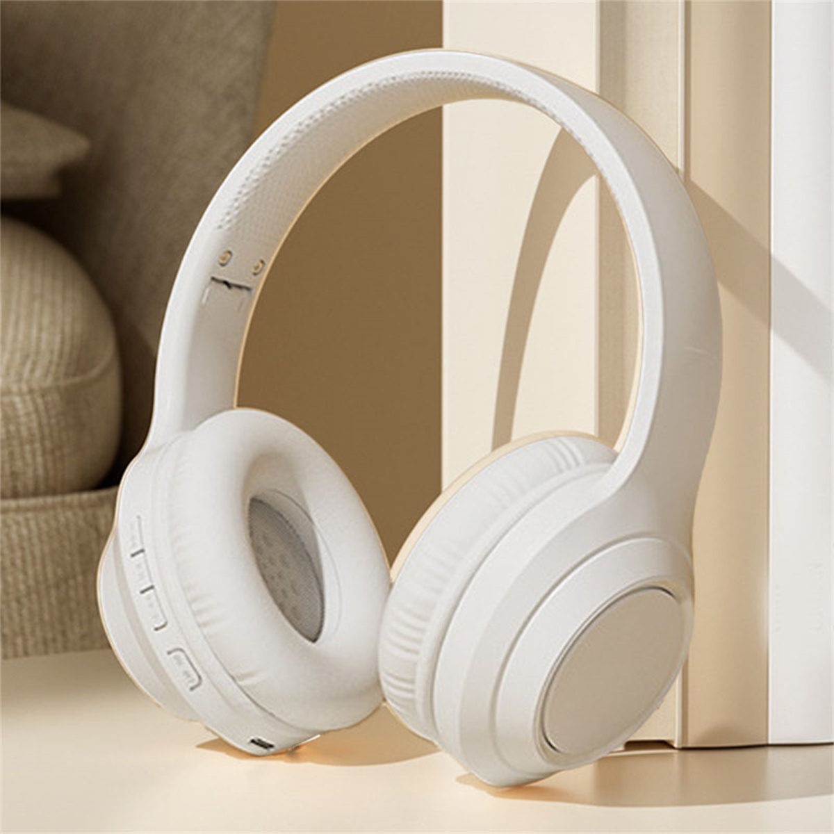 Weiße Over-Ear-Kopfhörer auf einem Tisch neben Büchern. Die Kopfhörer haben Knöpfe und ein weiches Design.
