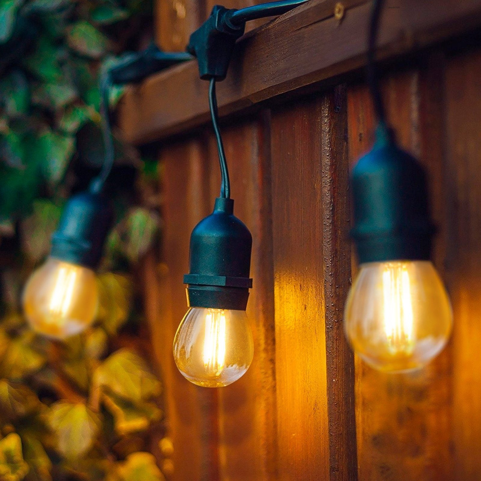 Trzy zapalone zewnętrzne lampki sznurkowe na drewnianym płocie. Ujęcie z bliska.