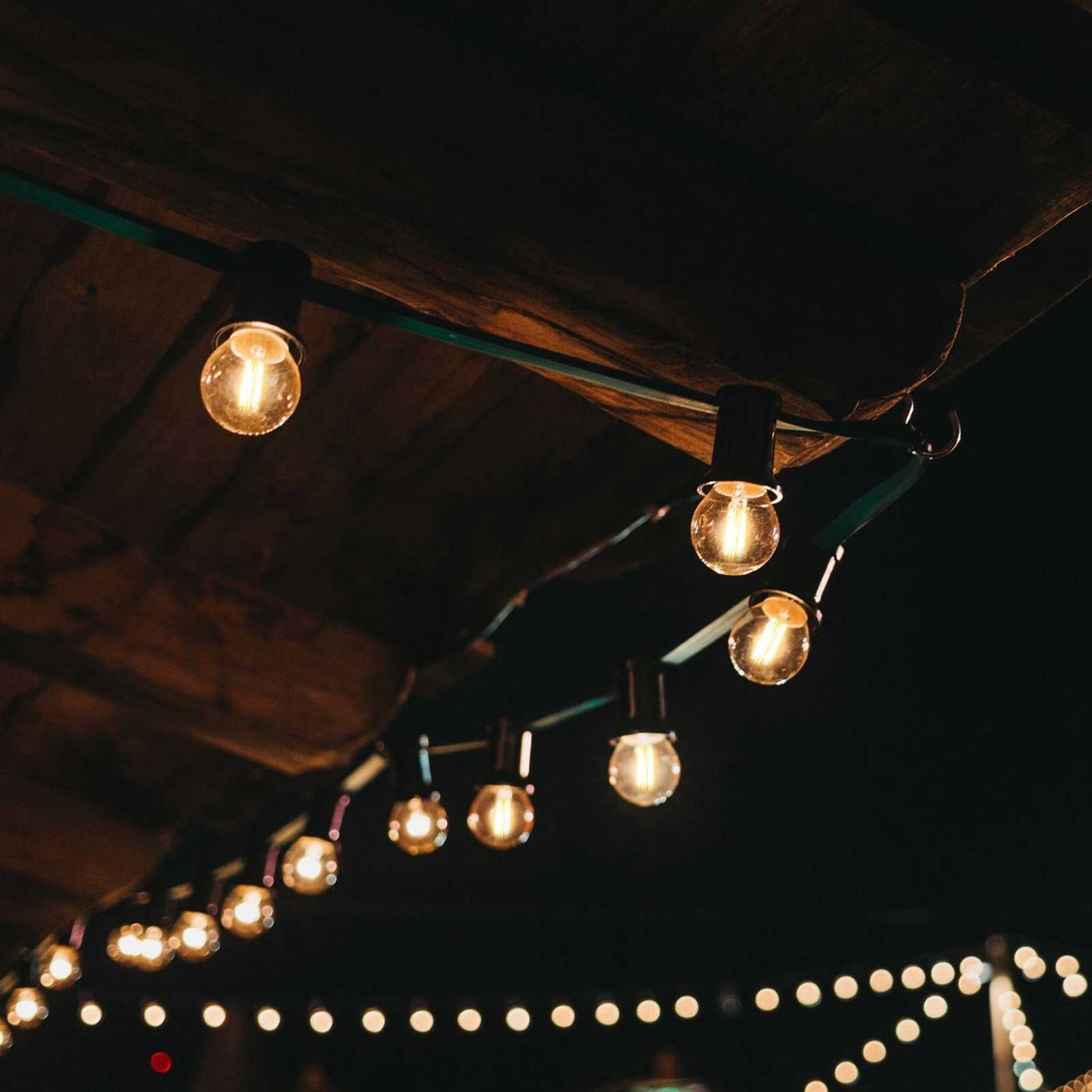 Lampki sznurkowe z żółtymi żarówkami wiszą nocą na drewnianej konstrukcji.