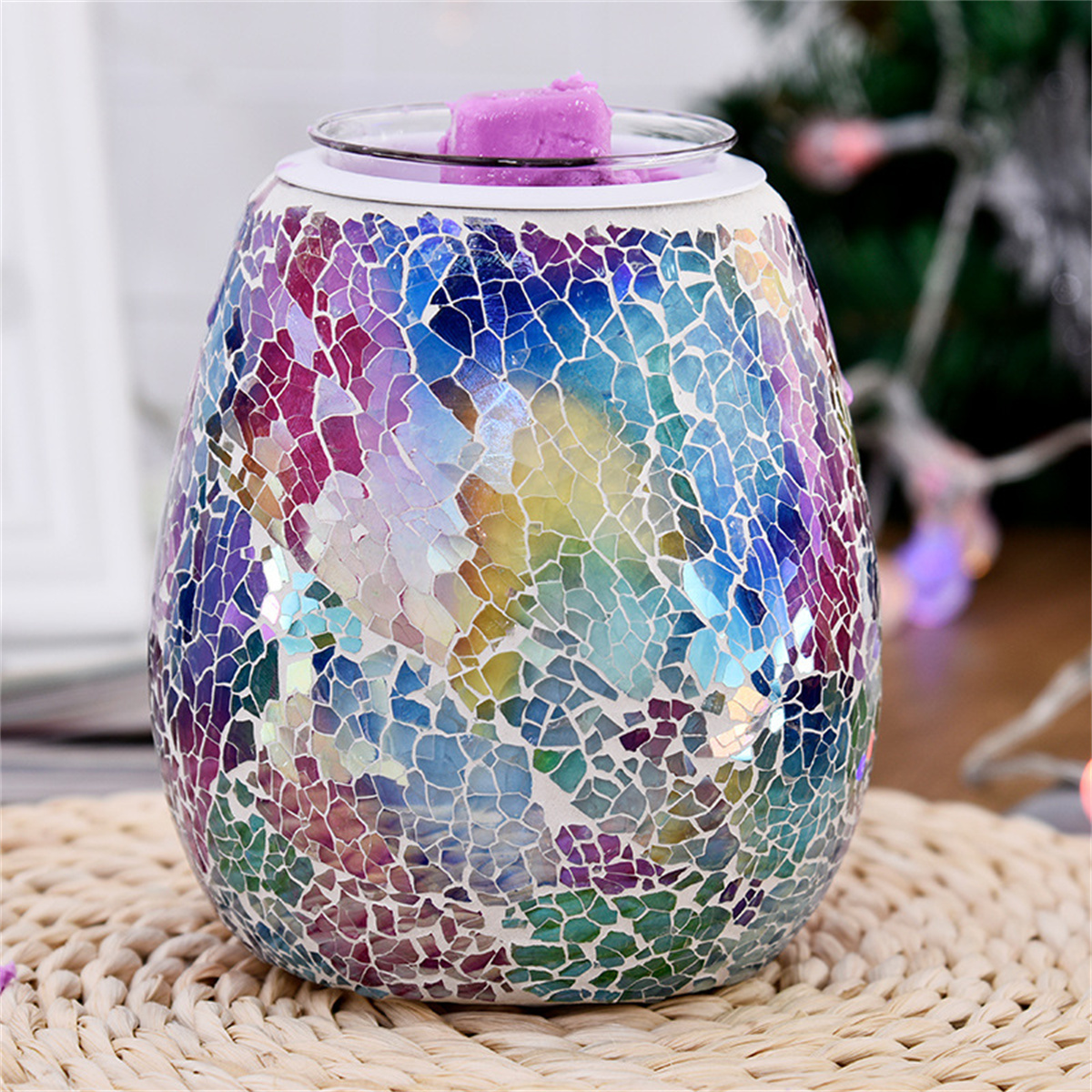 Ein bunter Mosaik-Wachswärmer mit einem lila Wachs-Schmelzstück, auf einer gewebten Matte.