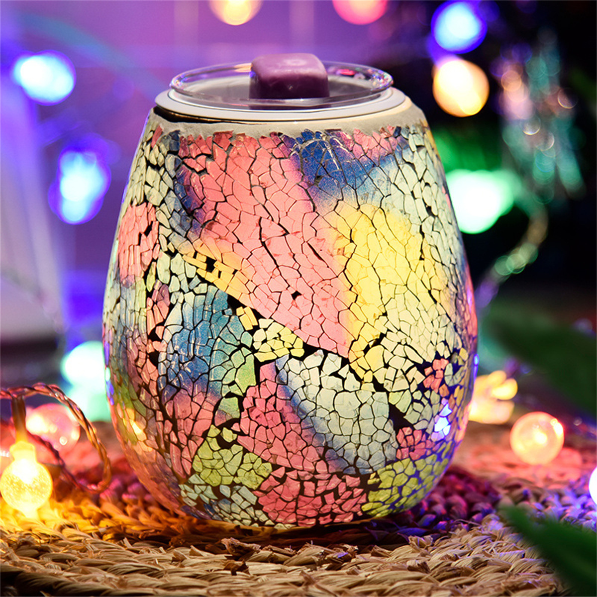 Glasbehälter im Mosaikstil mit Deckel. Es hat bunte Muster. Im Hintergrund befinden sich Lichter auf einer braunen Oberfläche.