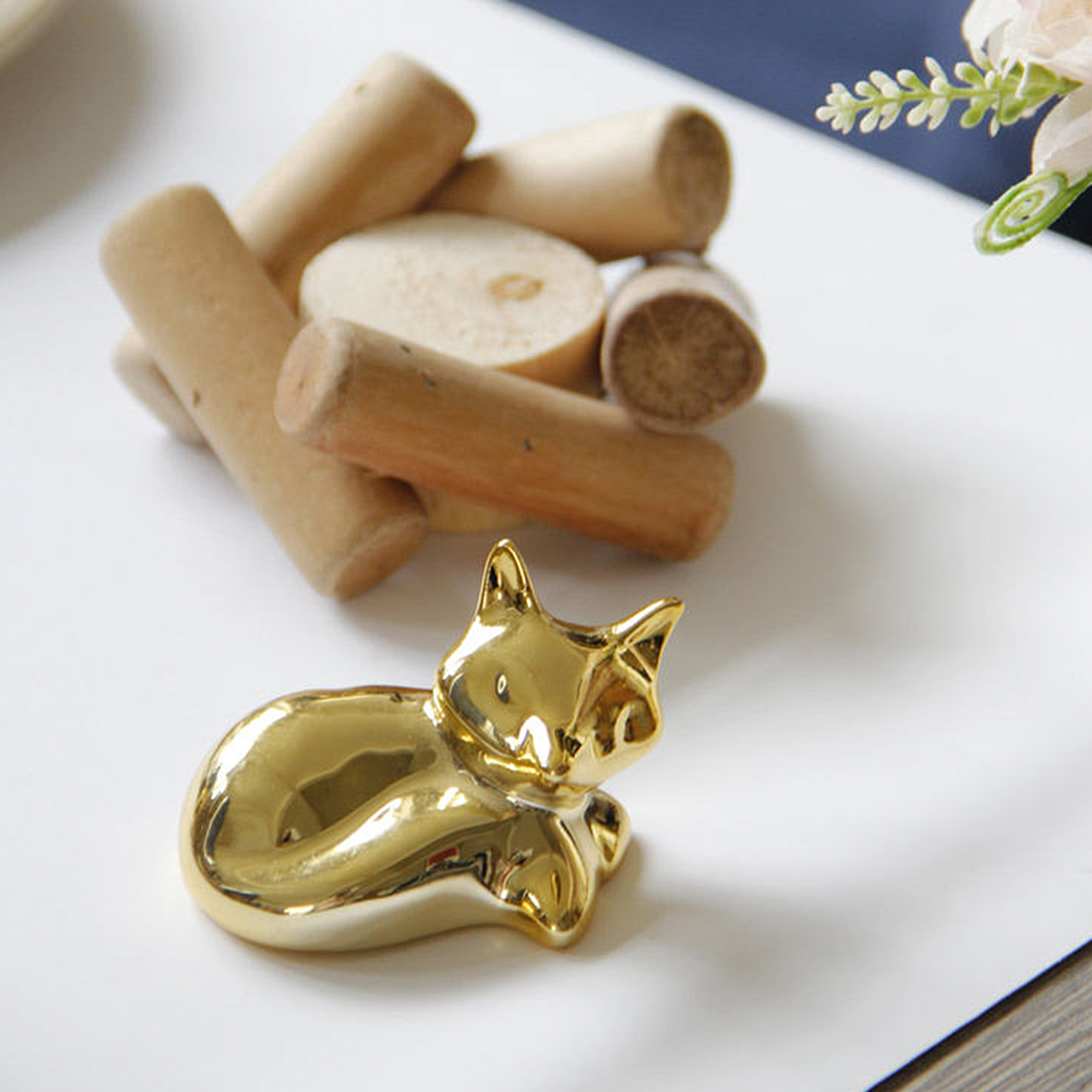 Goldenes Katzenornament und Holzzylinder auf weißer Oberfläche.