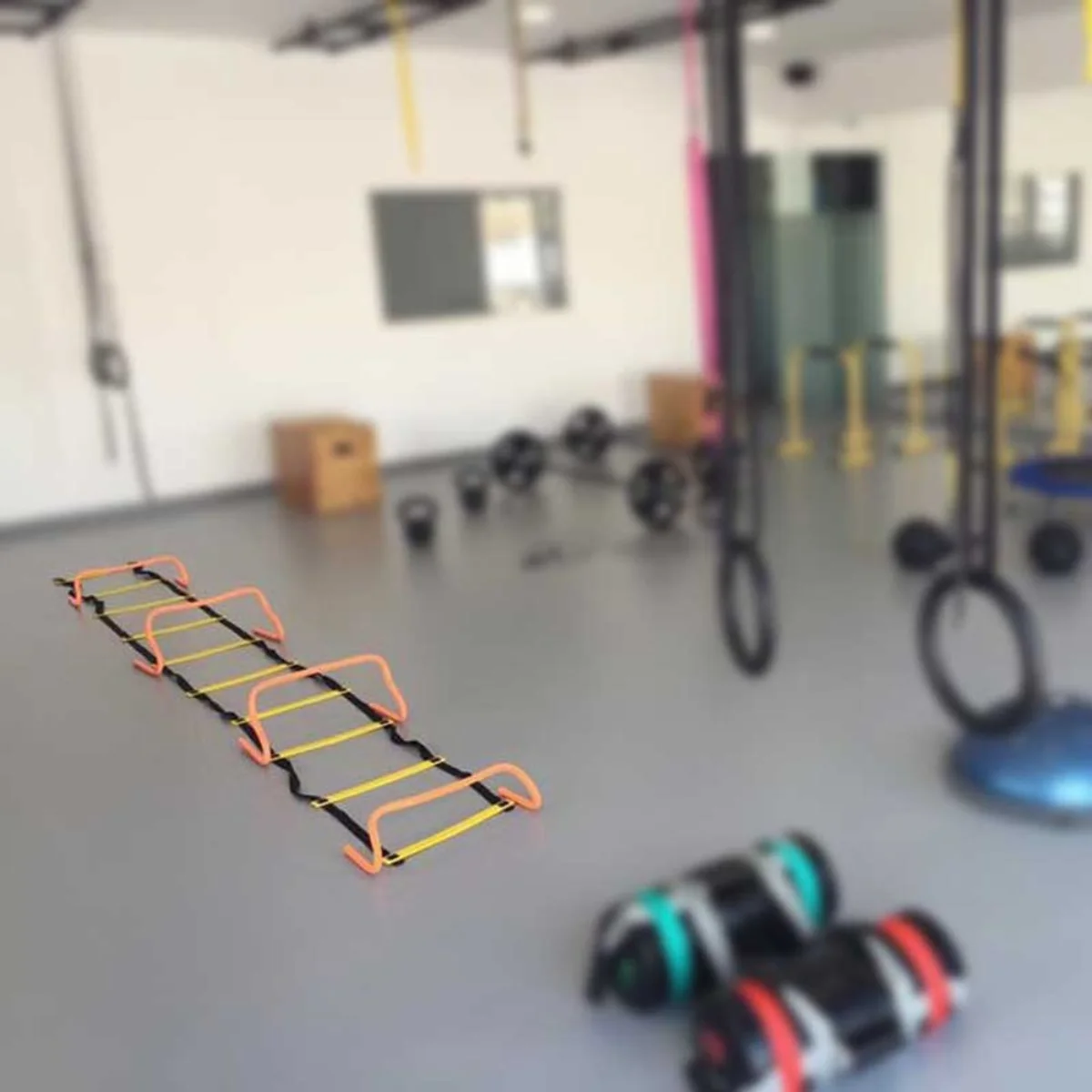 Une échelle de vitesse au sol dans une salle de sport, entourée d'équipements d'entraînement.