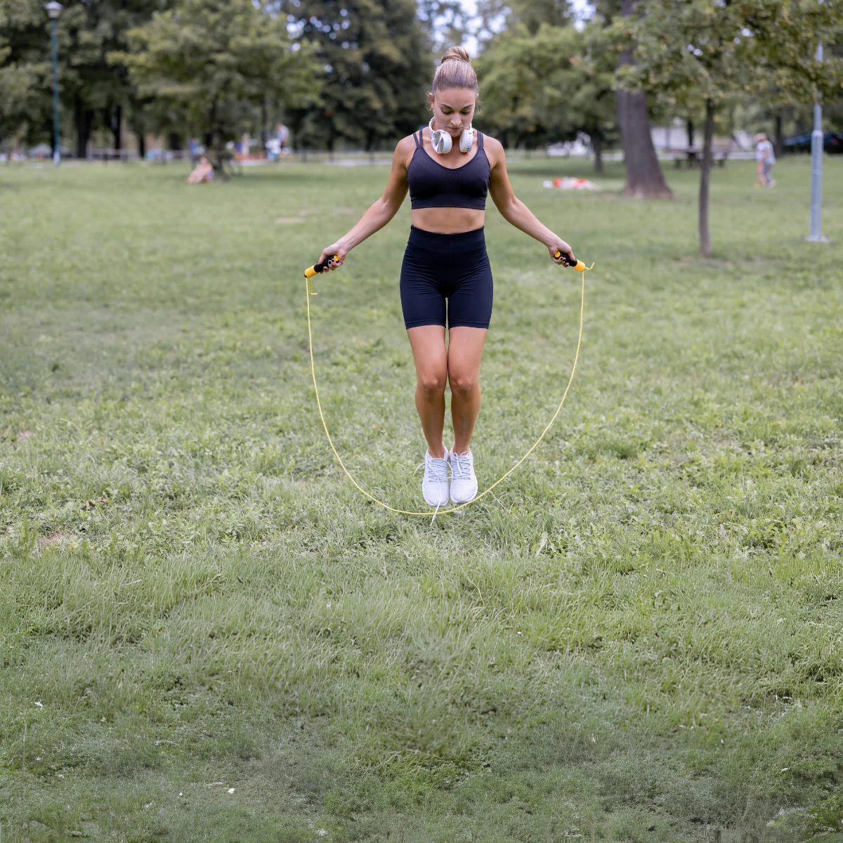 Vrouw die touwtje springt in een park, draagt zwarte sportkleding en witte schoenen.