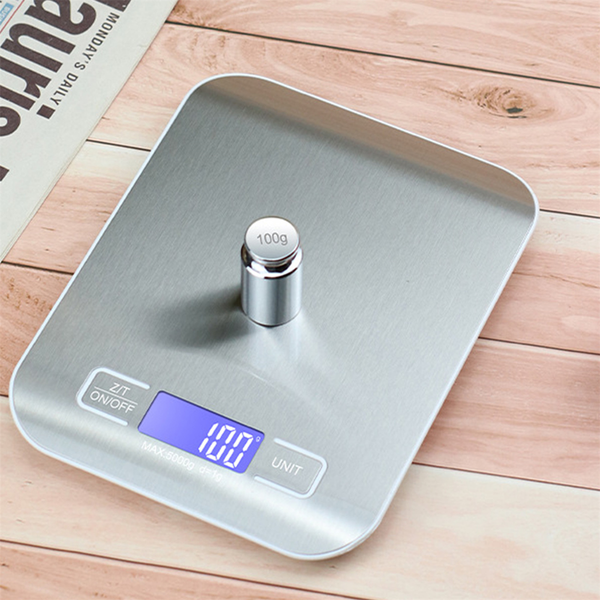 Eine digitale Küchenwaage mit einem 100g-Gewicht darauf, auf einer Holzoberfläche.