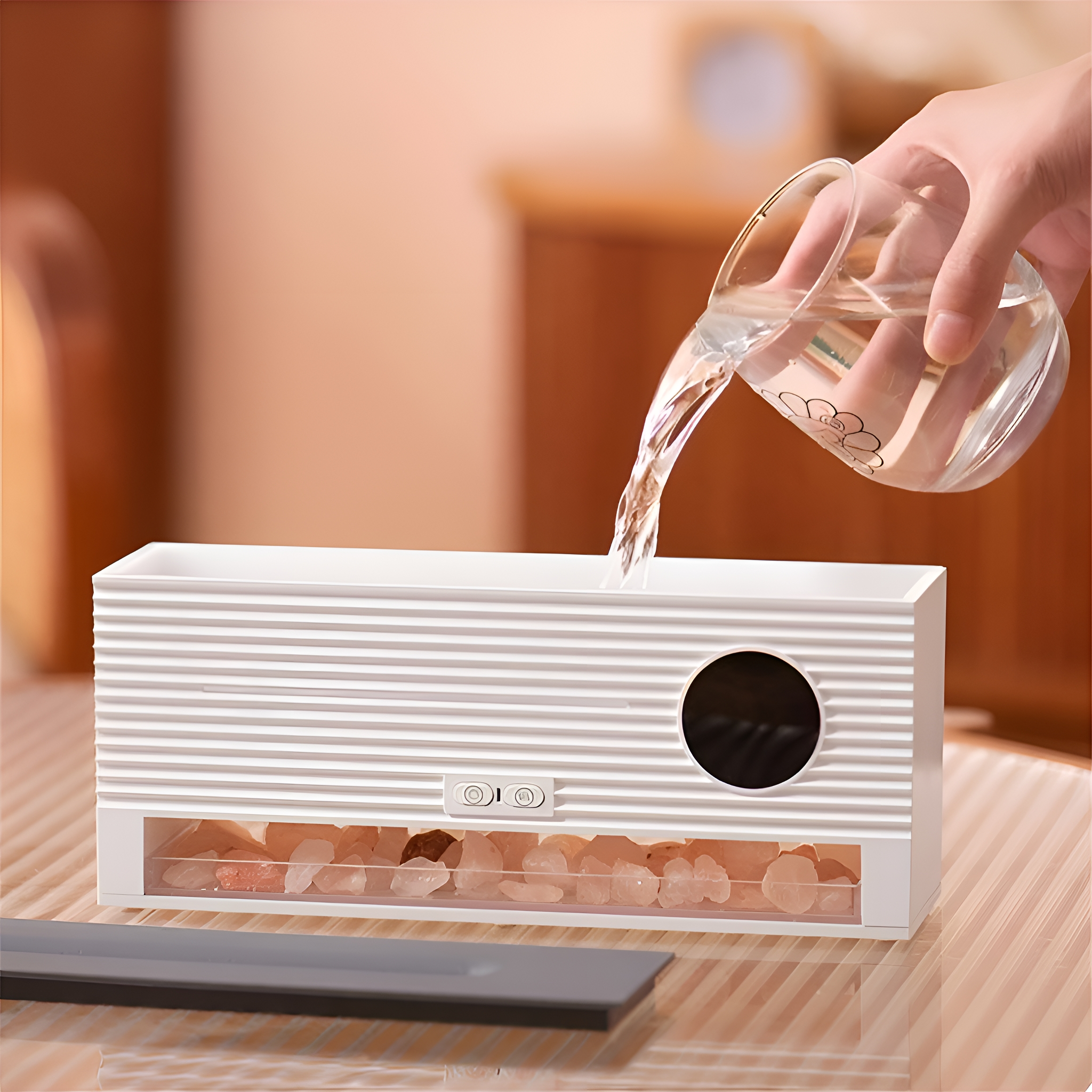 Weißer Luftbefeuchter mit Wasserguss; Steine am Boden, auf einem Glastisch.