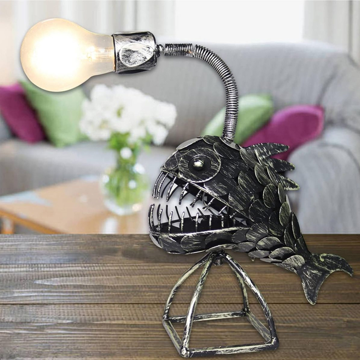 Eine metallene fischförmige Lampe mit Glühbirne auf einem Holztisch, heller Hintergrund.