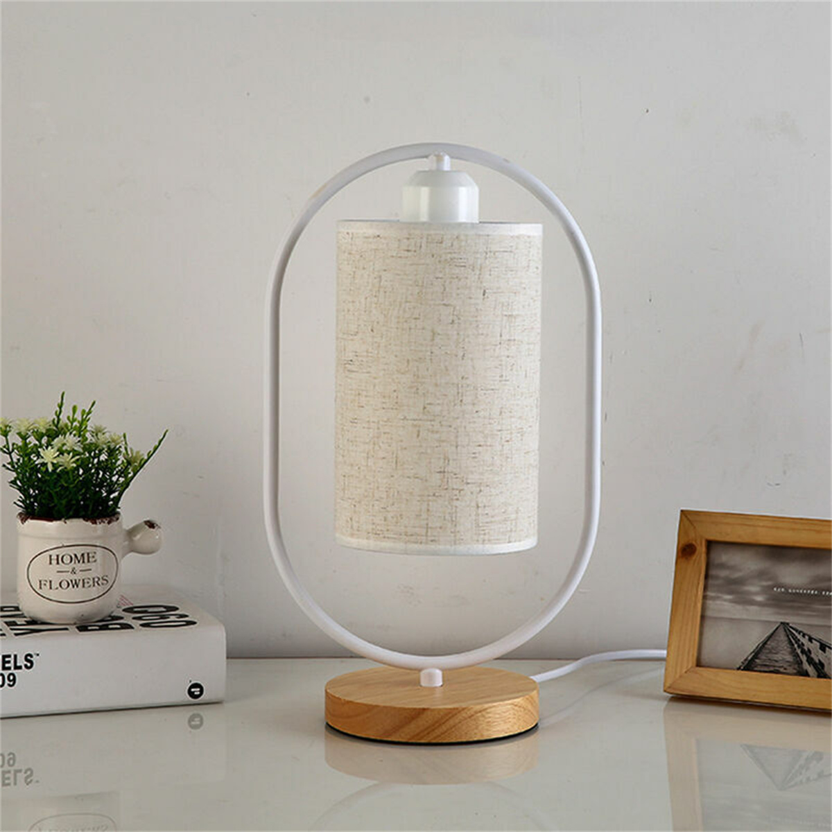 Eine weiße und hölzerne Tischlampe mit Stoffschirm, die auf einer weißen Oberfläche steht.
