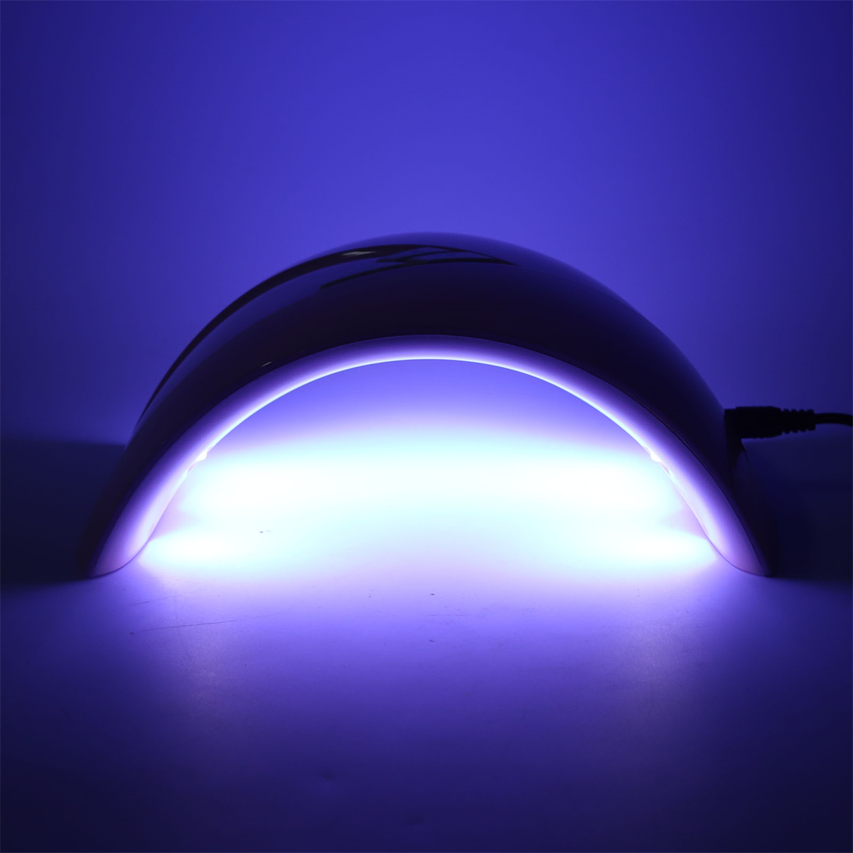 Eine violette UV-Lampe zum Aushärten von Nägeln, die blaues Licht aussendet. Dunkler Hintergrund.
