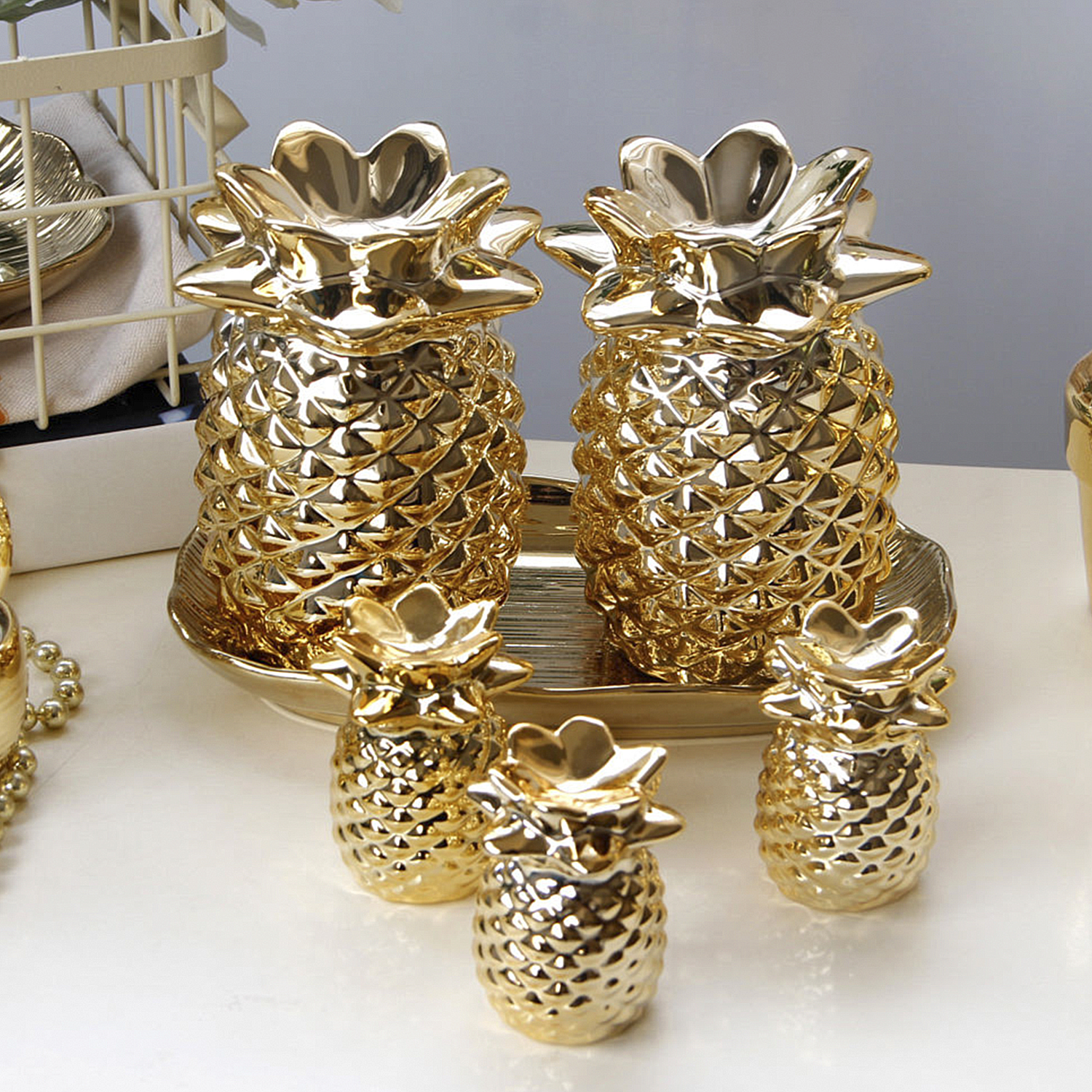 Decorazioni dorate a forma di ananas, su un vassoio e su una superficie bianca.