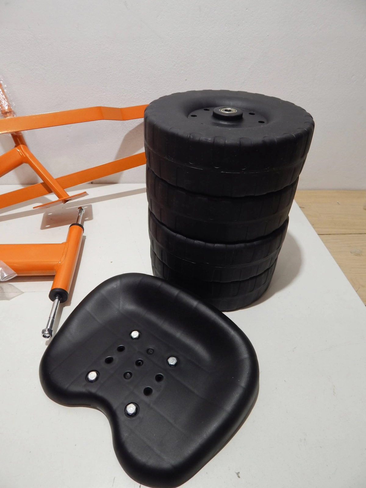 Eine Sammlung schwarzer Räder, ein schwarzer Sitz und ein orangefarbener Rahmen, möglicherweise für ein Go-Kart oder ähnliches Fahrzeug.