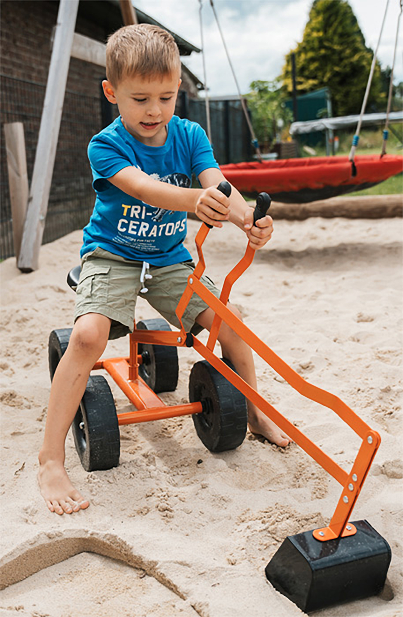Ein kleiner Junge spielt mit einem Spielzeugbagger in einem Sandkasten, im Hintergrund eine Schaukel.