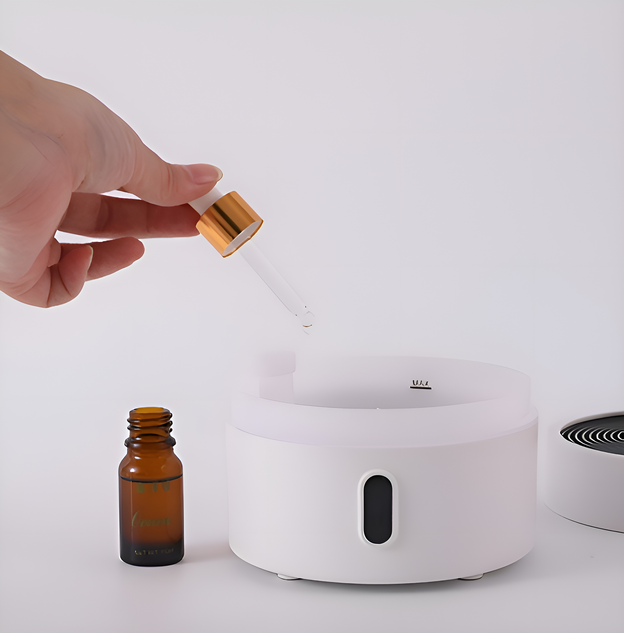Eine Hand hält eine Pipette über einem weißen Aromatherapie-Diffusor mit einer ätherischen Ölflasche.