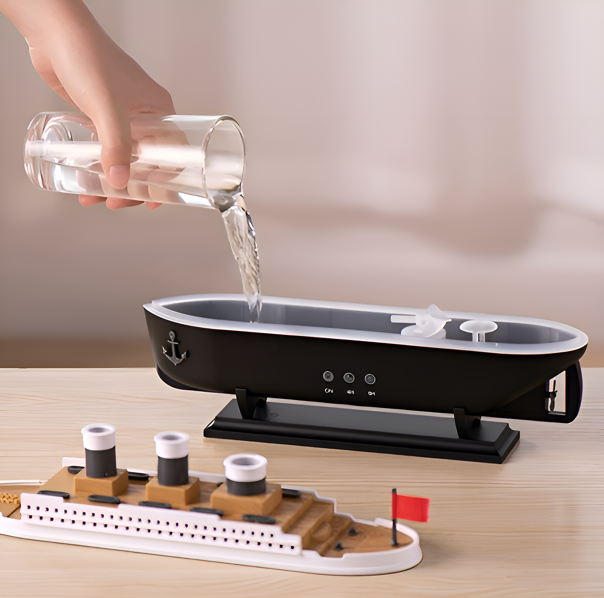 Eine Hand gießt Wasser in einen schwarzen, bootsförmigen Luftbefeuchter, im Vordergrund ein Modellschiff.
