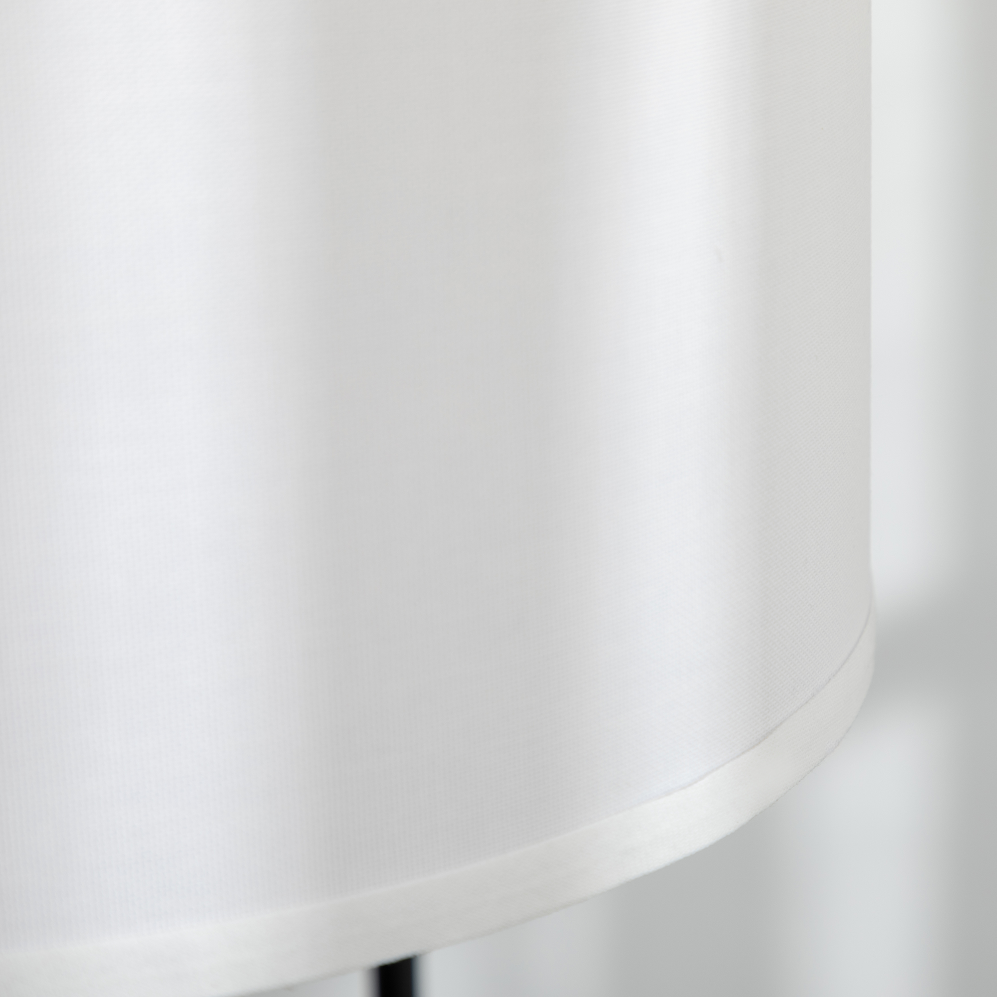 Primer plano de una pantalla de lámpara blanca con borde curvado, sobre un fondo blanco liso.