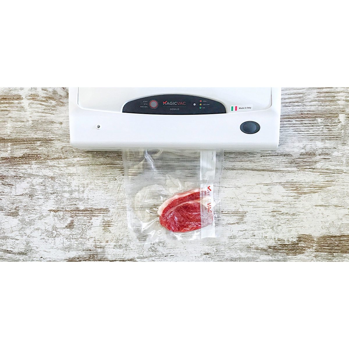Biała maszyna Magic Vac zamykająca kawałek surowego mięsa w przezroczystej torbie. Tło to drewniana powierzchnia.