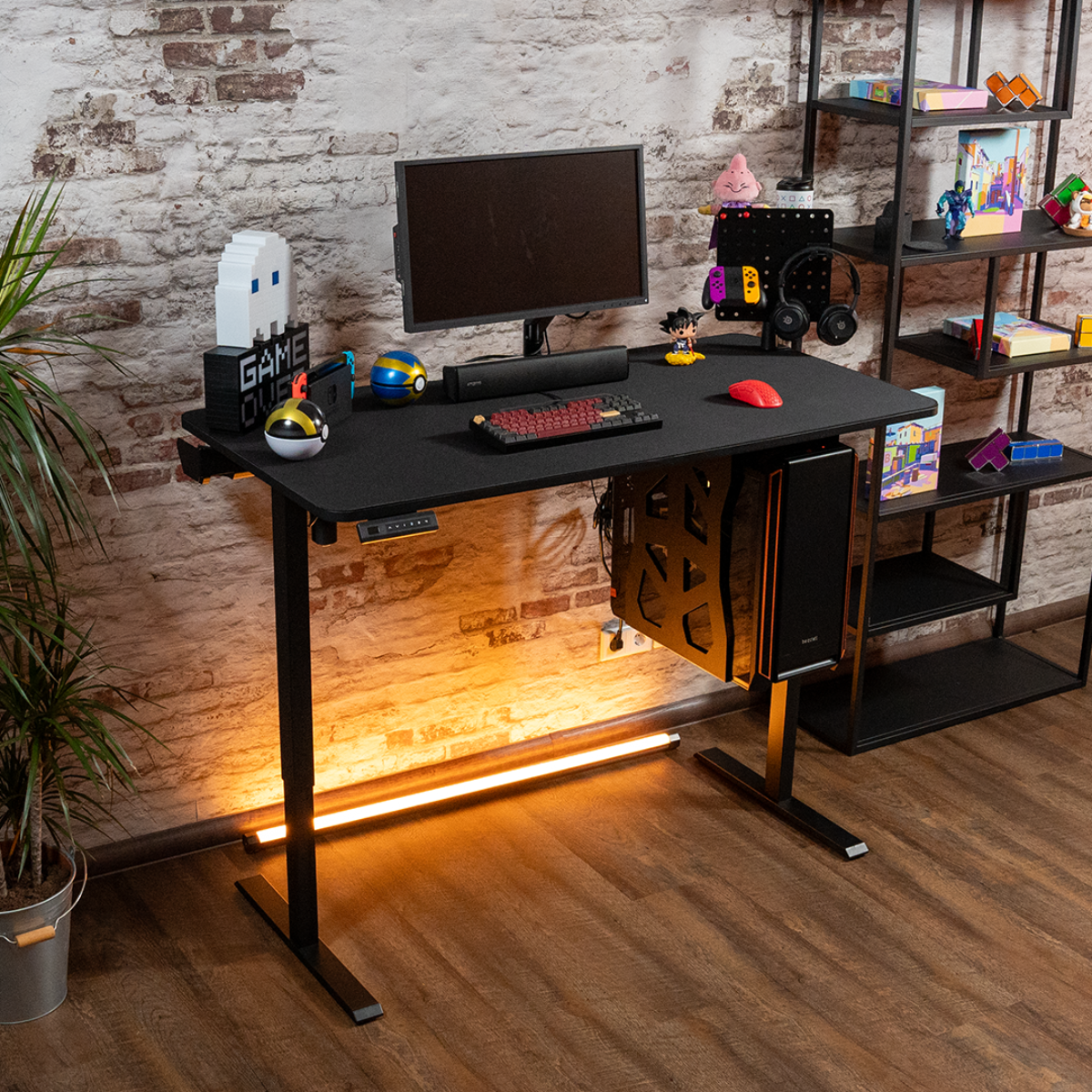 Ein Gaming-Schreibtisch mit PC, Monitor, Tastatur und Zubehör vor einer Ziegelmauer.