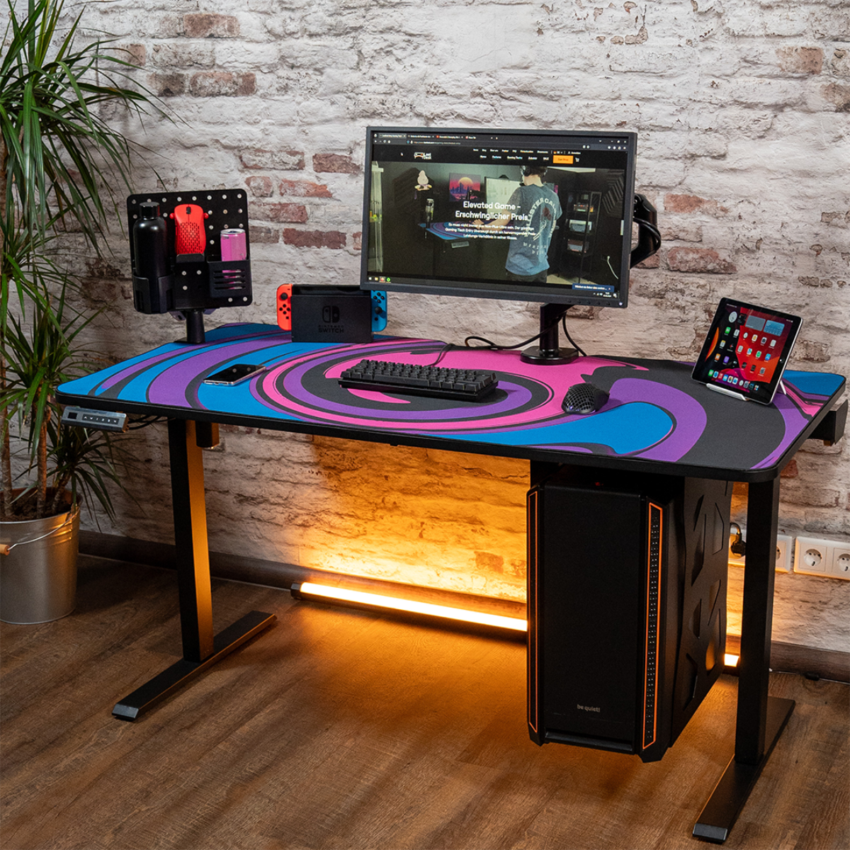Ein Gaming-Schreibtisch mit Computer, Monitor und Zubehör. Der Schreibtisch ist schwarz mit buntem Design.