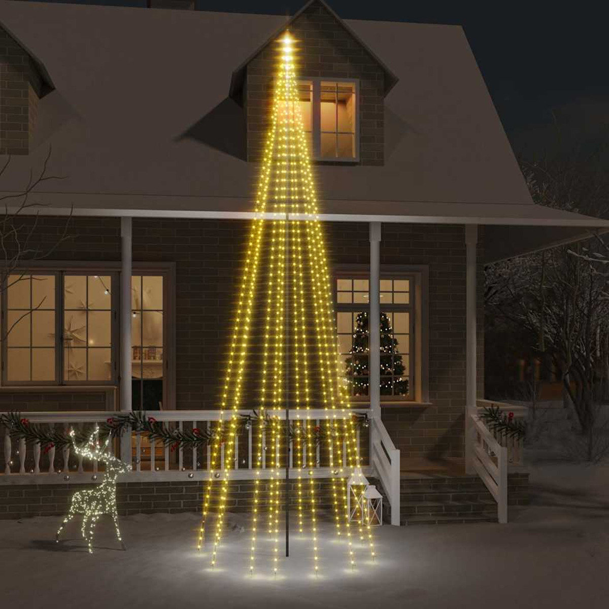 Ein Haus ist mit einem Weihnachtsbaum aus Lichtern beleuchtet. Eine Rentierdekoration liegt im Schnee.