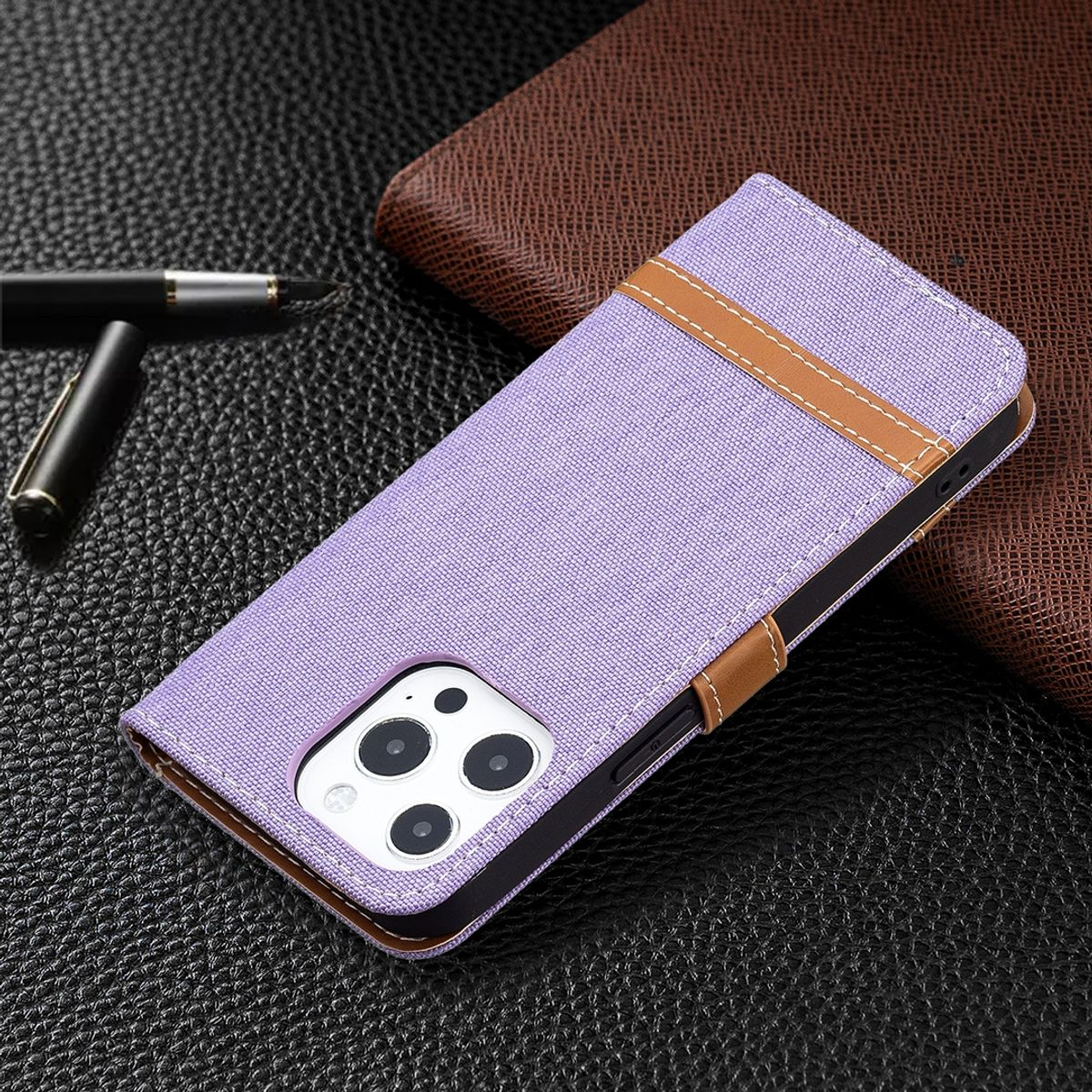 Violette Handyhülle mit braunem Riemen auf dunkler Oberfläche. Stift im Hintergrund, Leder-Notizbuch.