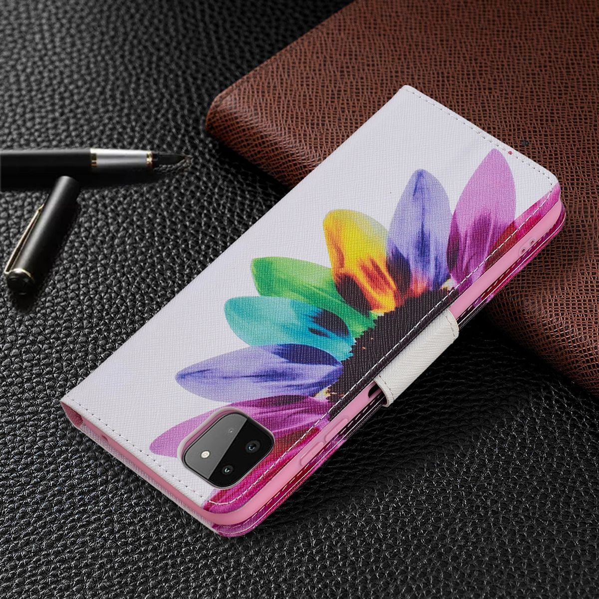 Eine Handyhülle mit buntem Blumendesign, mit einem schwarzen Stift und einer braunen Geldbörse.